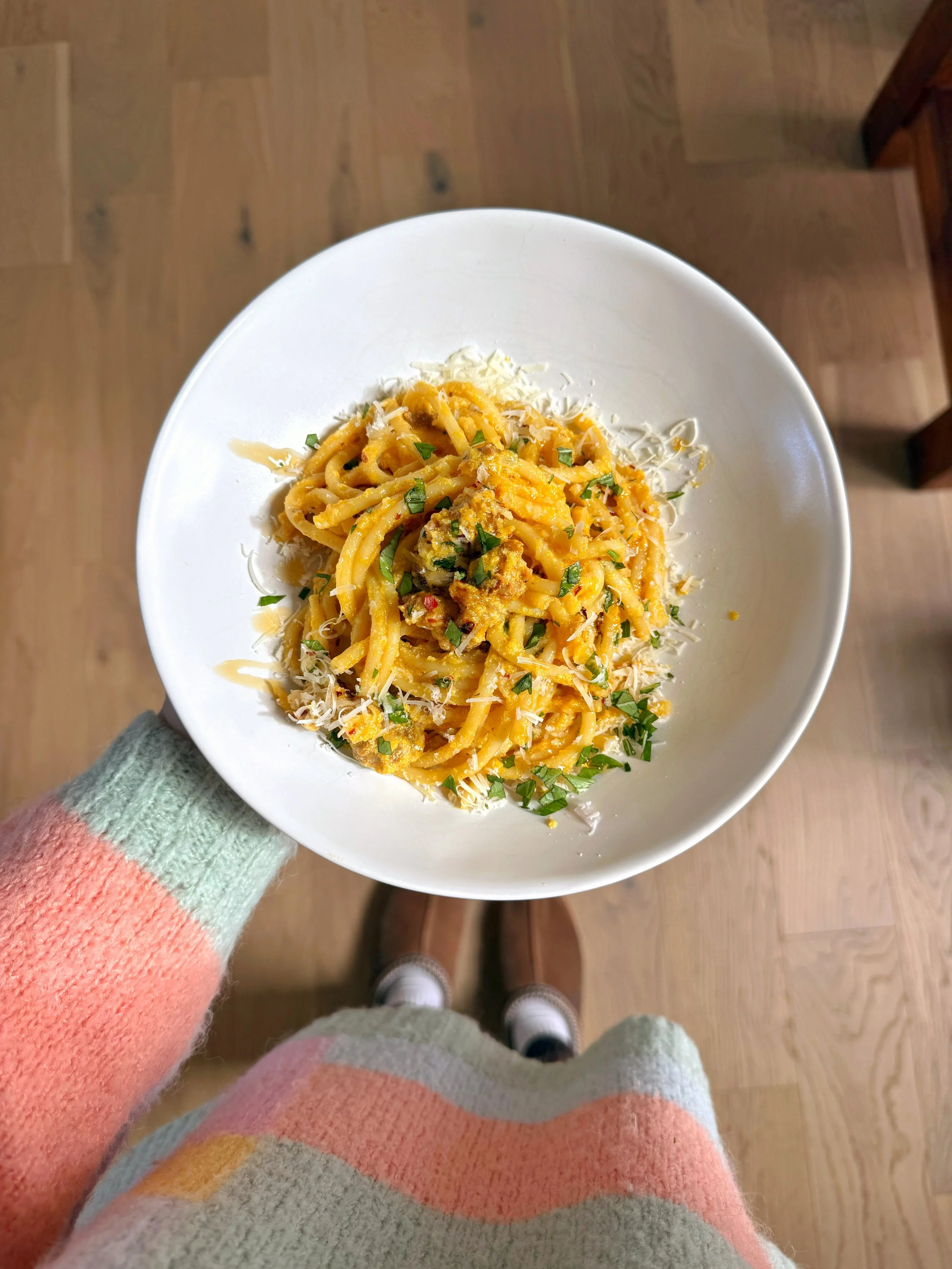 A bowl of creamy pumpkin Alfredo noodles with grated parmesan cheese and chopped basil on top.
