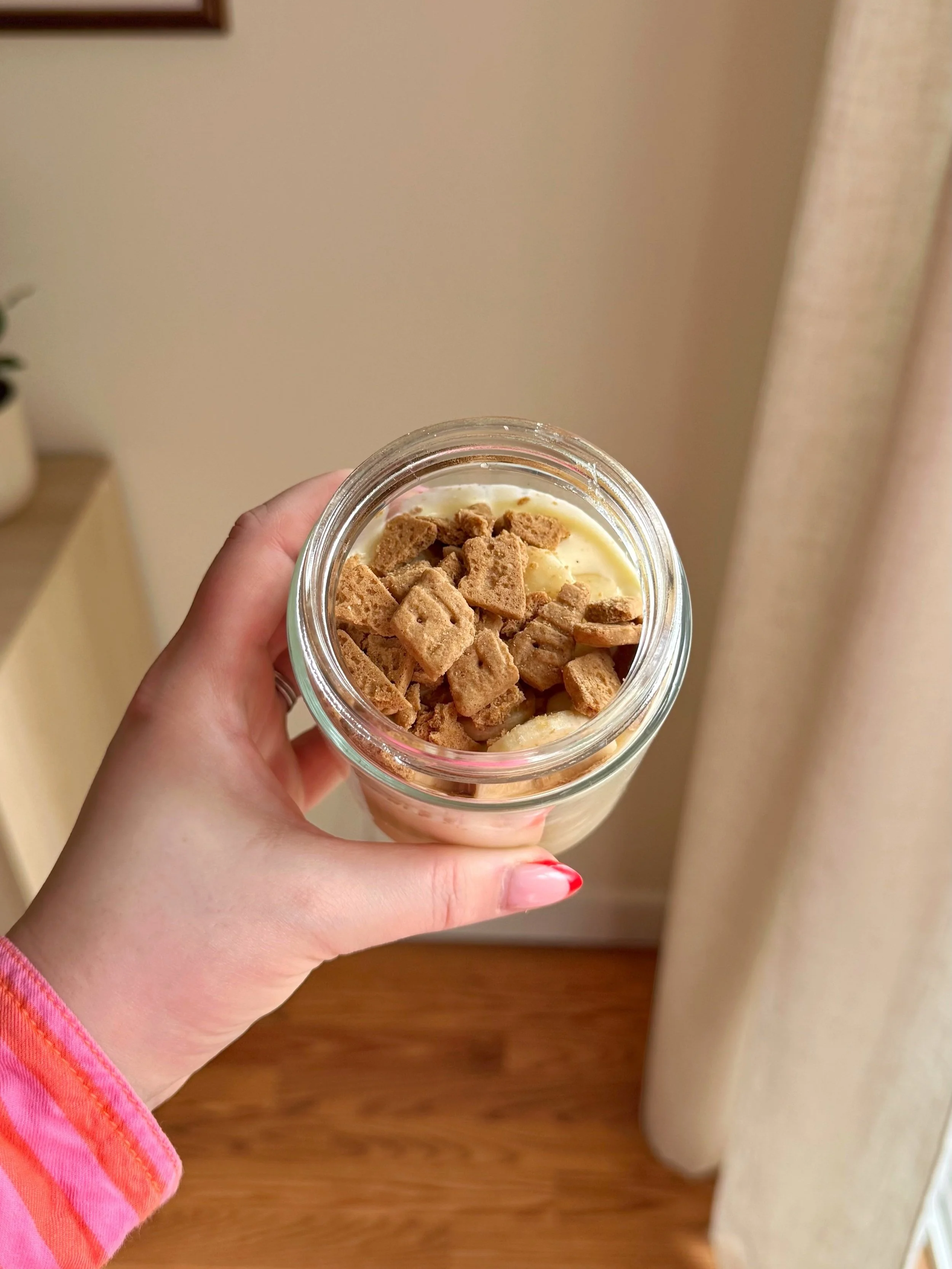 A jar of banana pudding with fresh bananas and crackers on top. 
