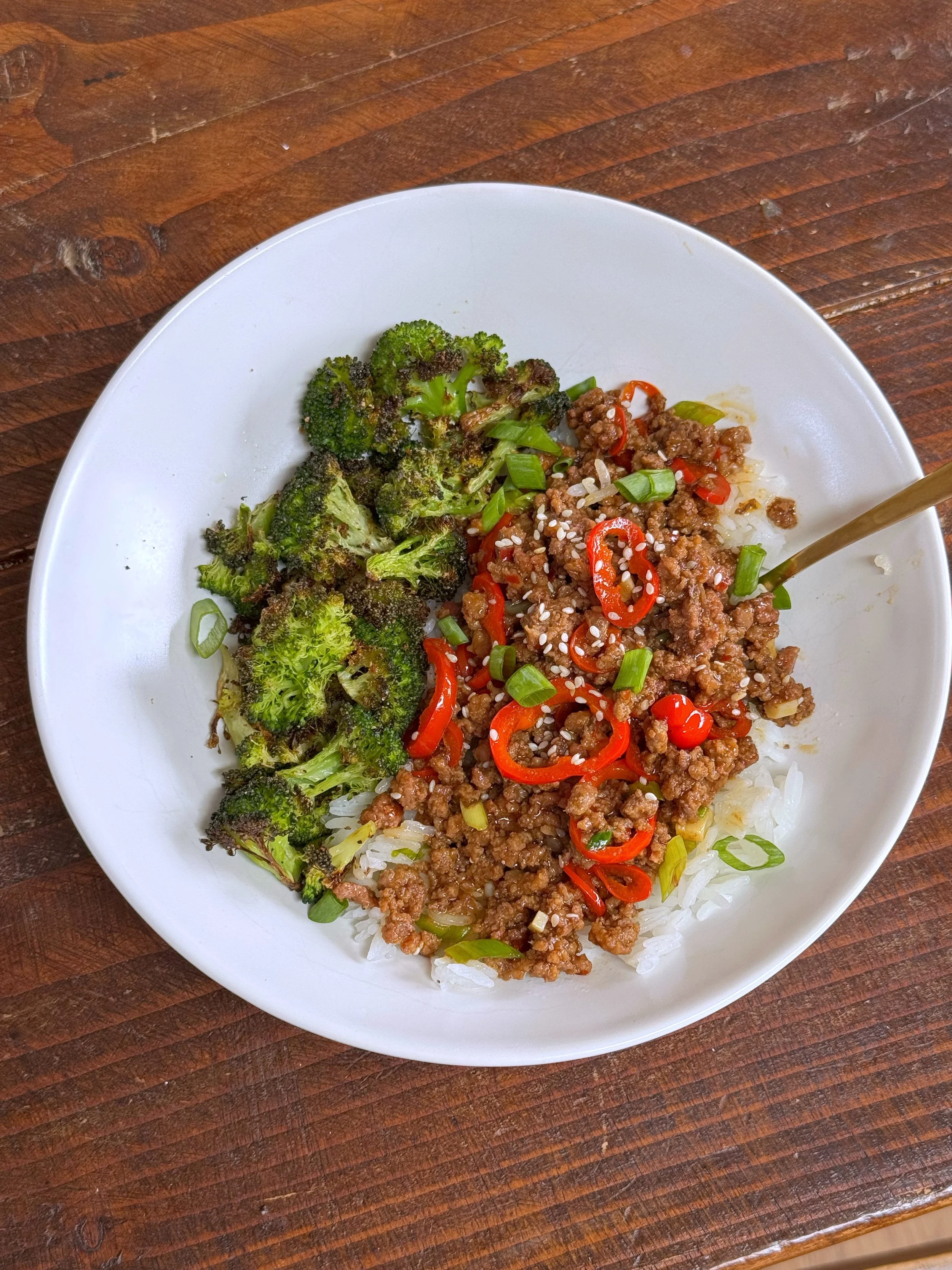 A bowl of ground beef and broccoli over rice topped with chopped green onions and sesame seeds.