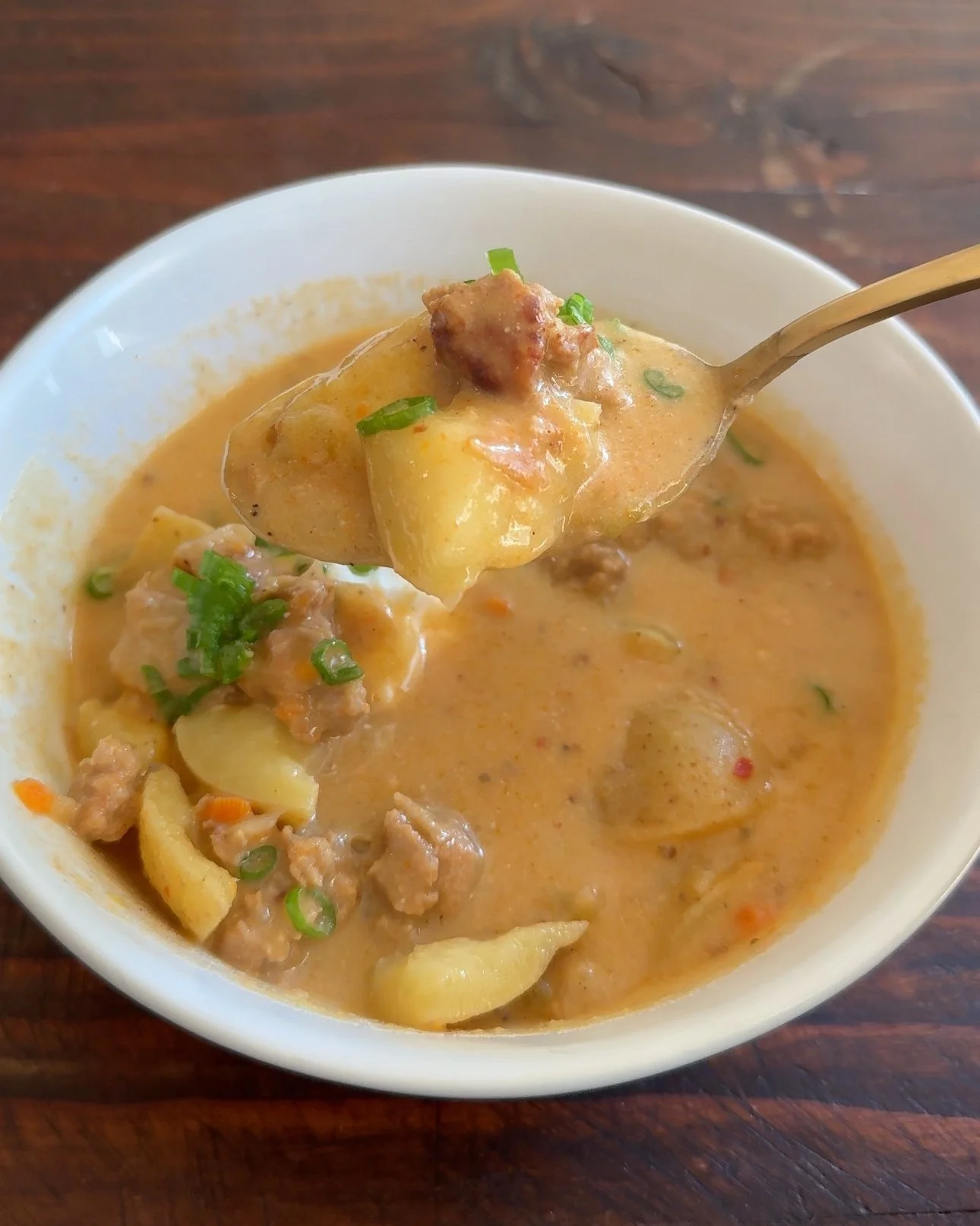 A bowl of potato chowder soup with sausage, sour cream and chopped green onions.