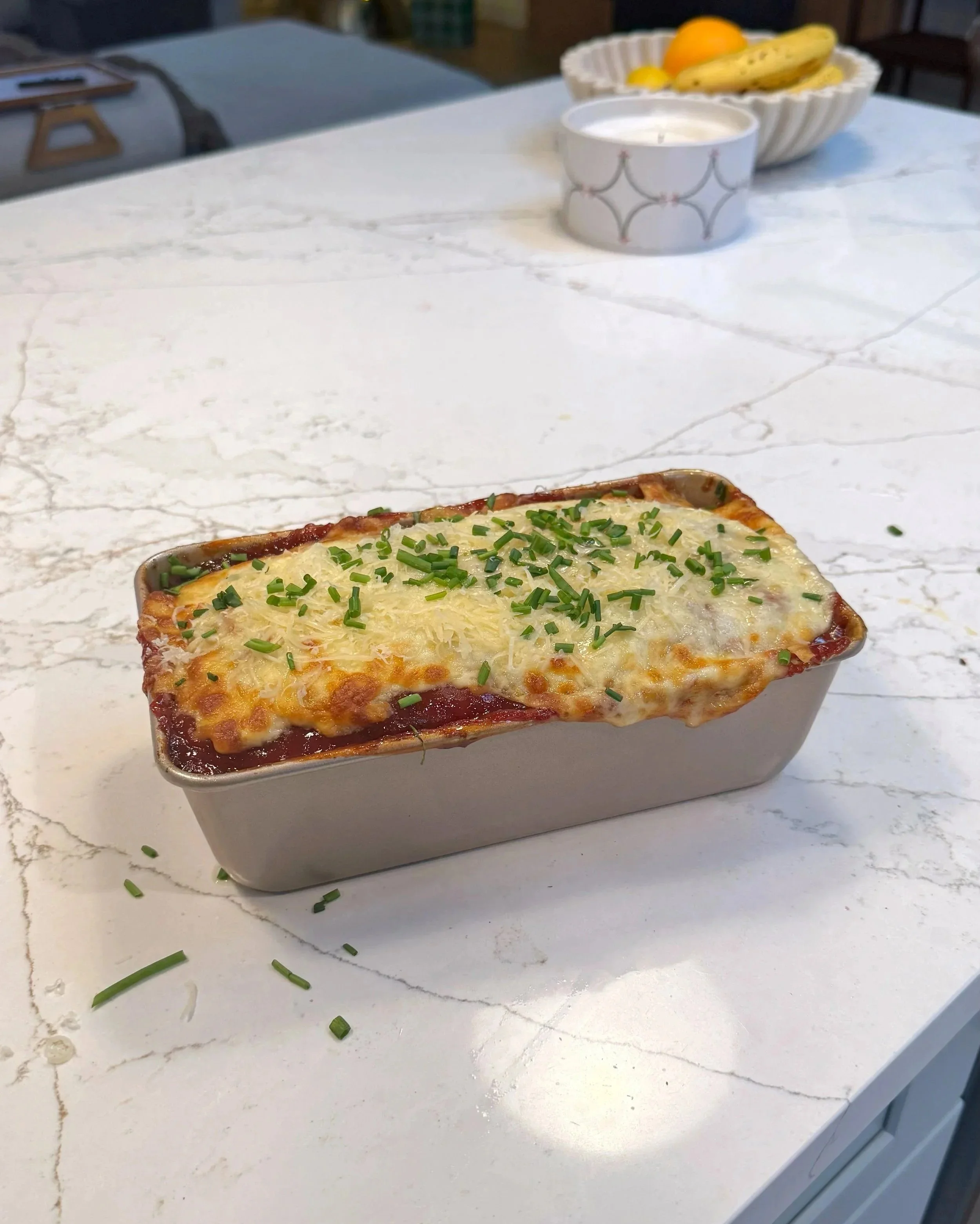 A pan of meatloaf with fresh chives on top siting on a counter. 