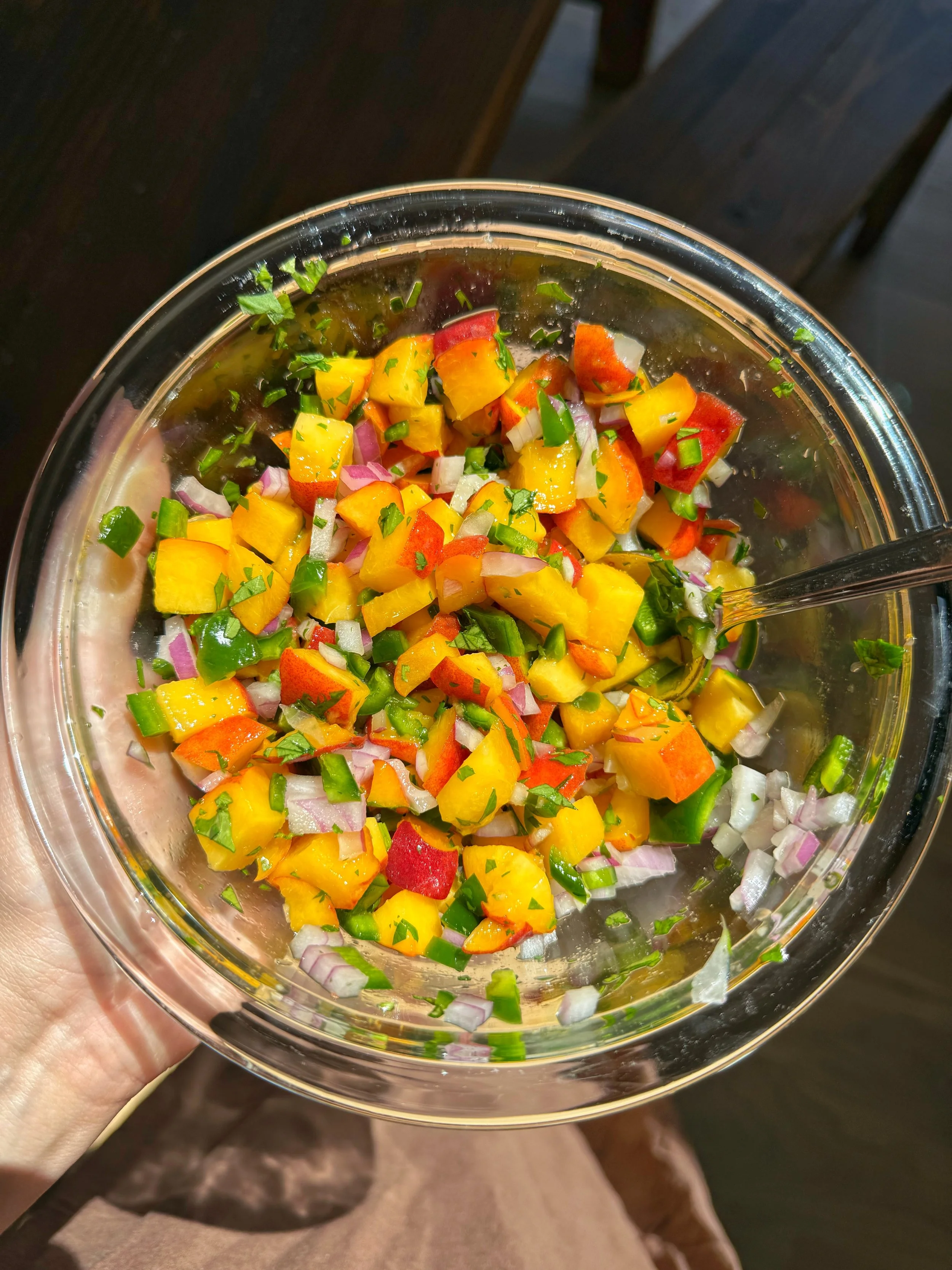 A bowl of salsa that has cut up peaches, jalapeños, red onion, & chopped cilantro.