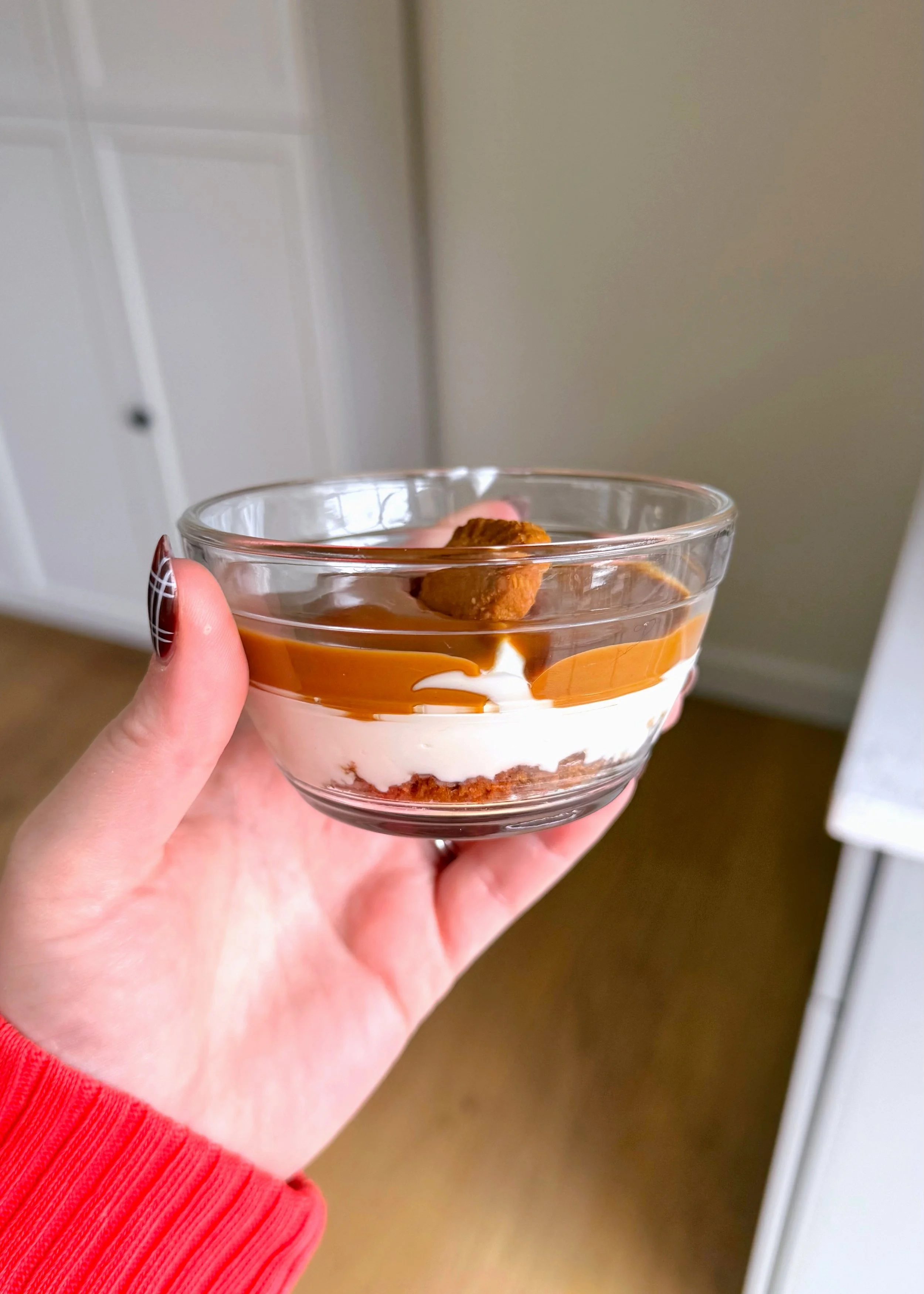 Little glass bowl with a cookie crumble crust and cream like cheesecake with melted Biscoff and a Biscoff cookie on top. 