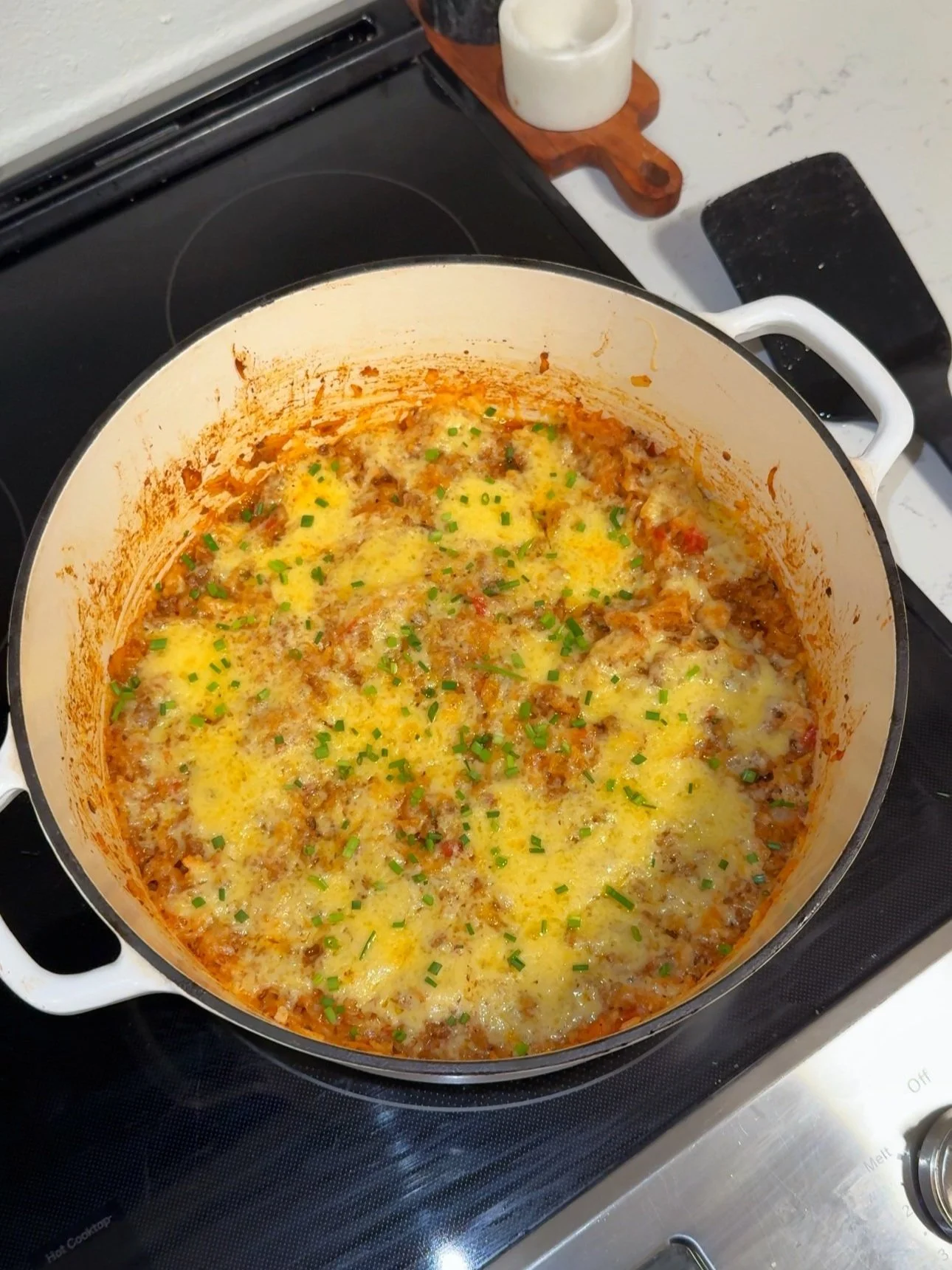 A pot on the stove with ground beef, rice, gouda cheese and chopped chives on top. 