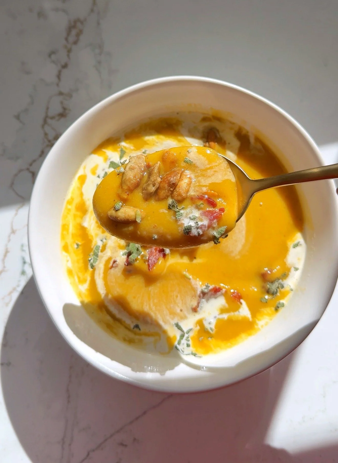 A close up shot of a bowl of butternut squash soup with drizzle of cream, bacon bits and toasted pumpkin seeds on top.