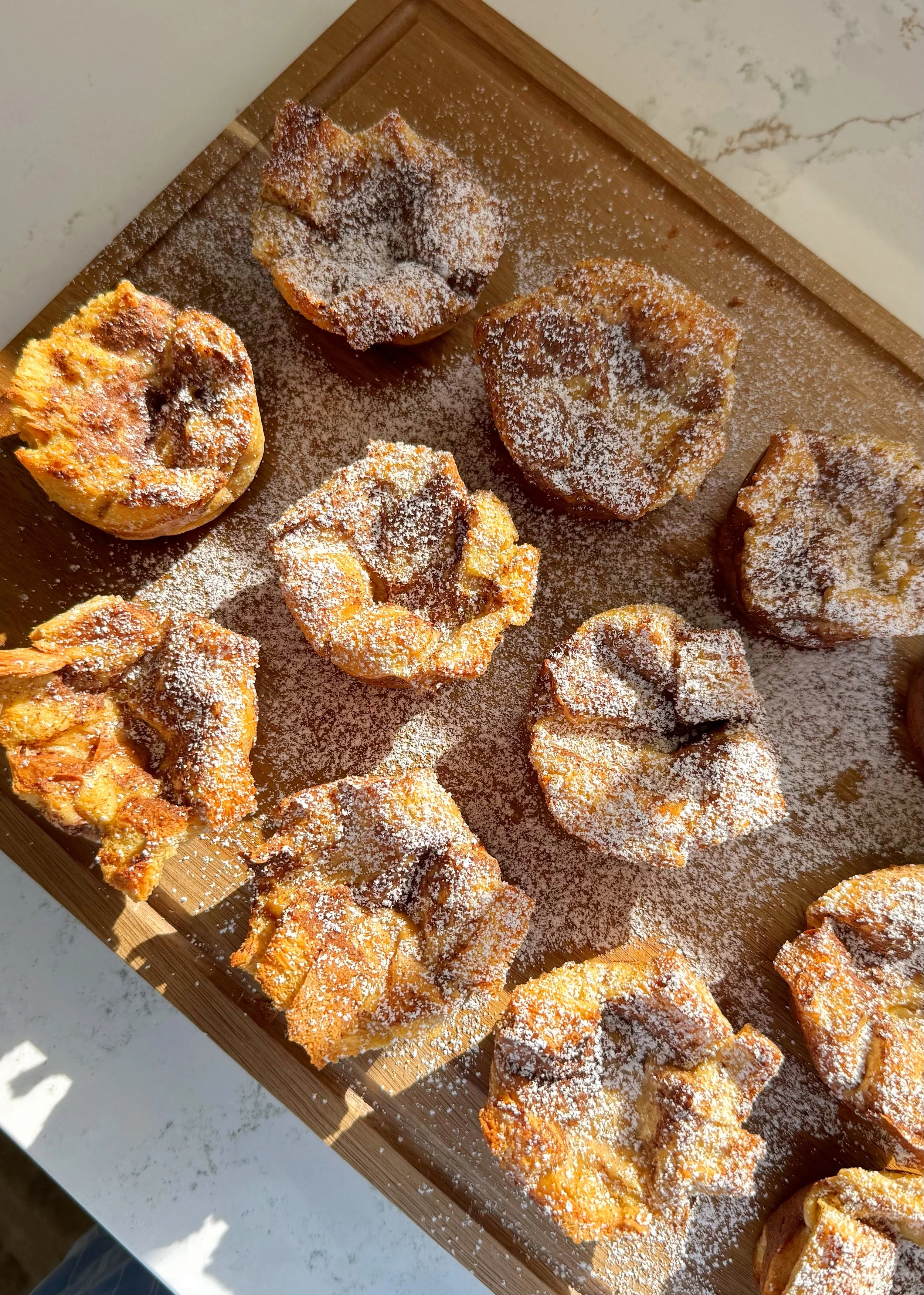 French toast cups with powered sugar sprinkled on top sitting on a cutting board.