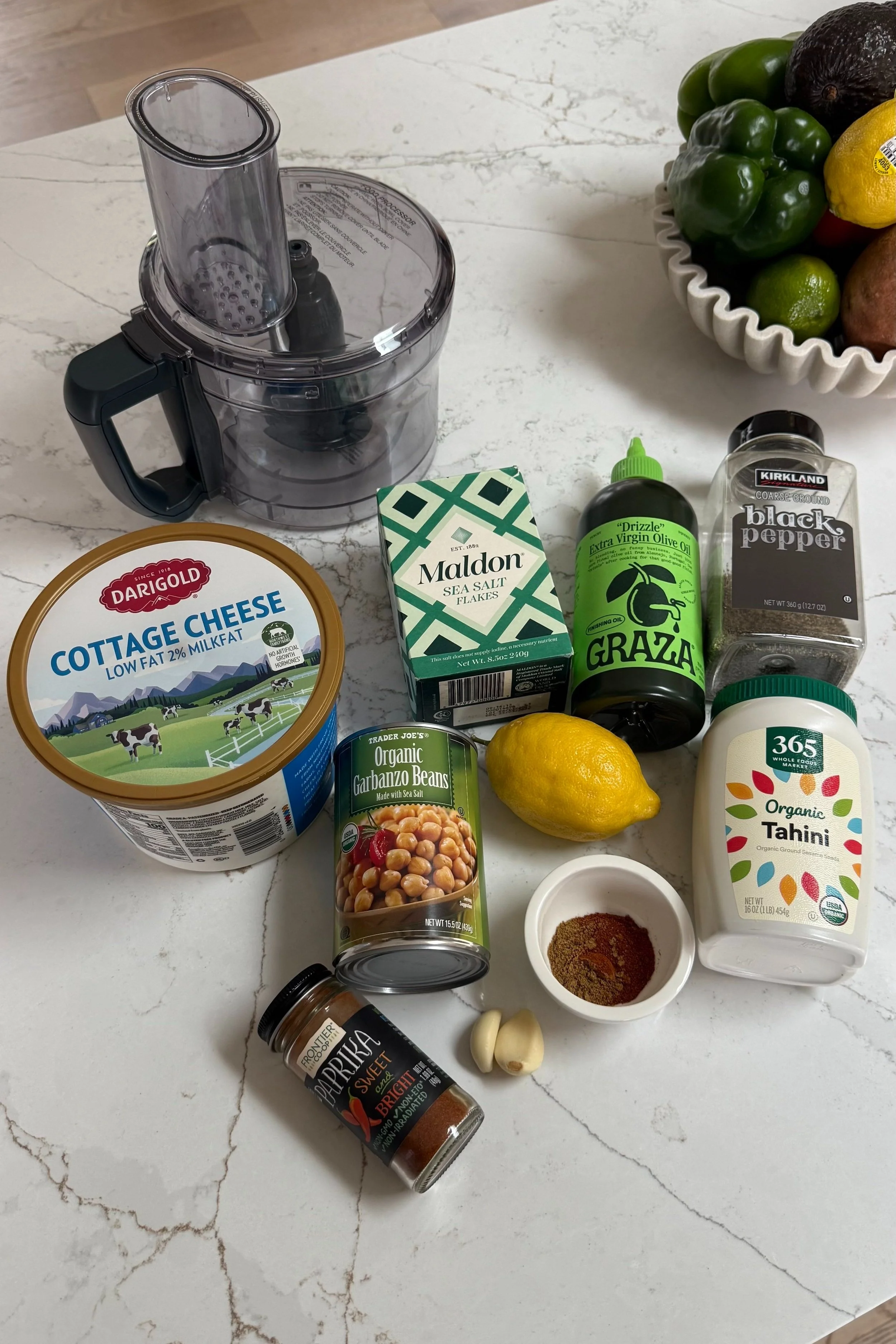 All the ingredients to make the hummus sitting on a countertop sitting next to a food processor.