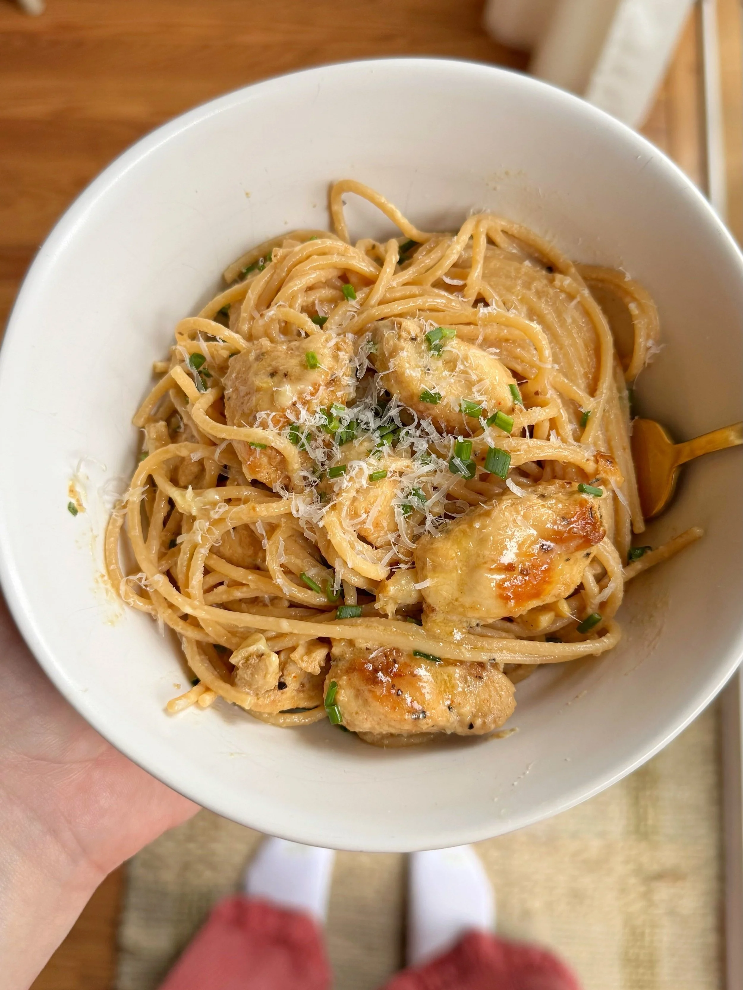 A bowl of noodles & lemon chicken with fresh chives and grated cheese on top.