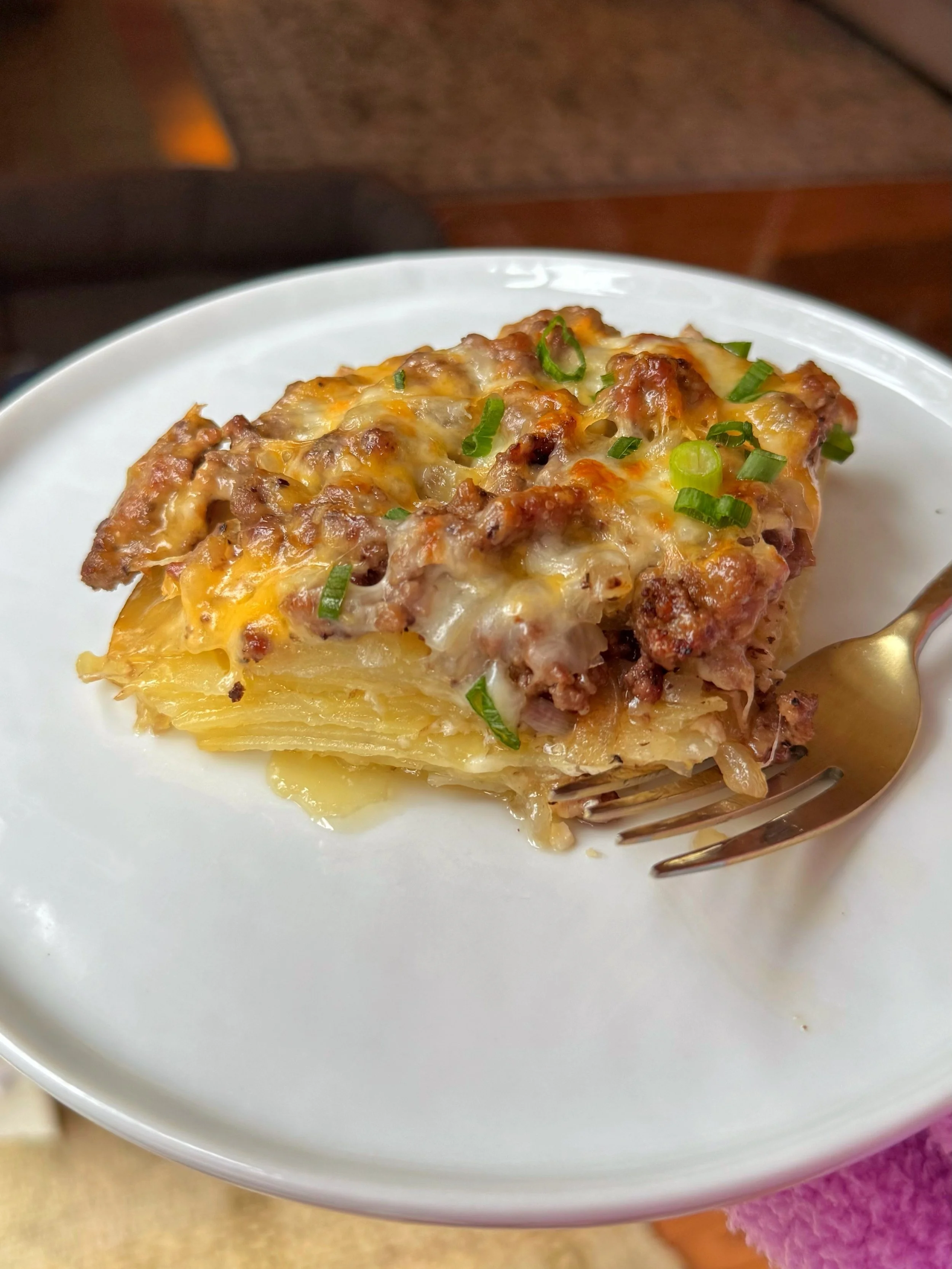 A plate with cheesy potatoes and beef topped with chopped green onions.