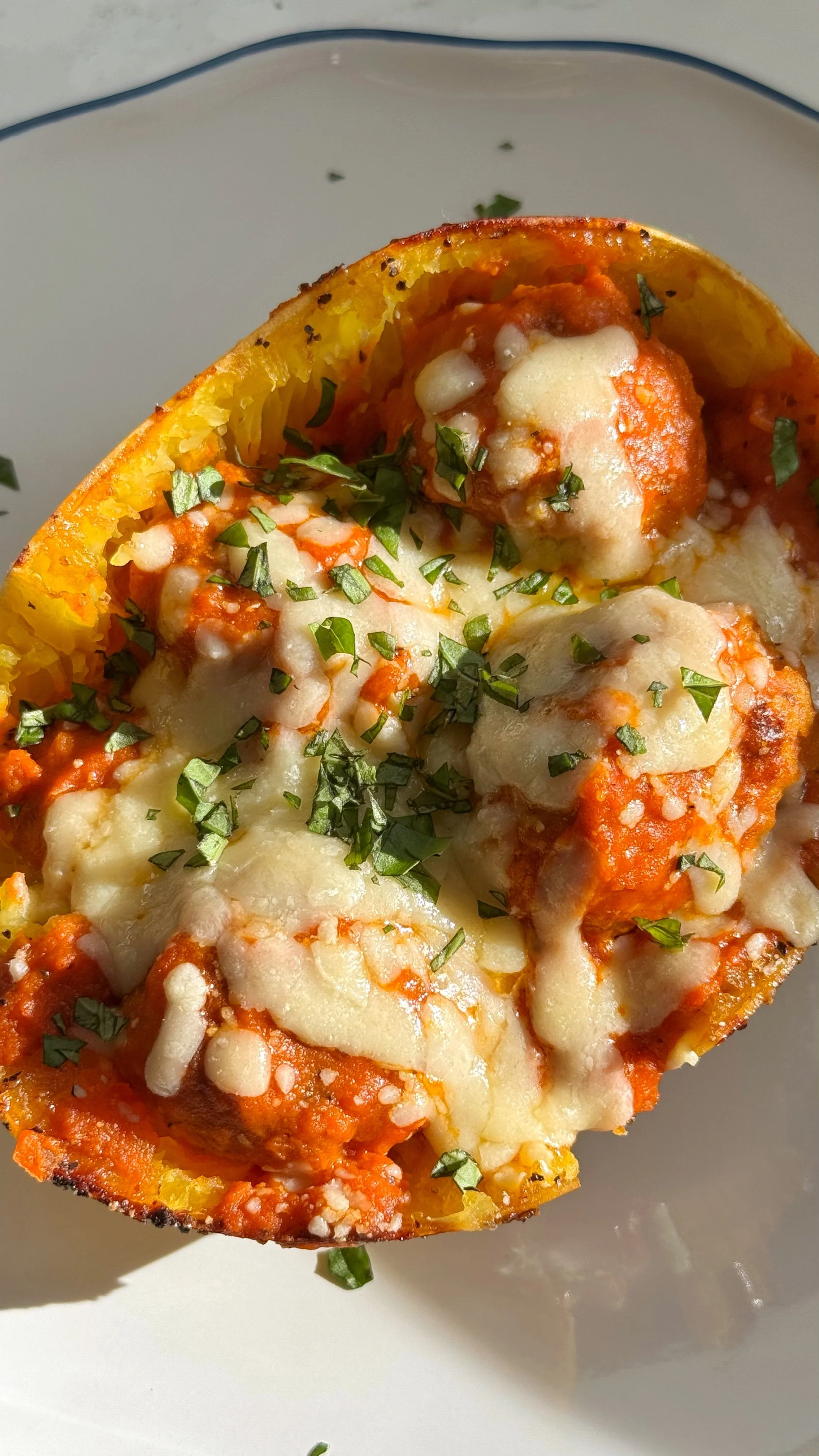 A close up shot of a spaghetti squash boat filled with ground chicken with marinara sauce topped with melted cheese and fresh chopped basil. 