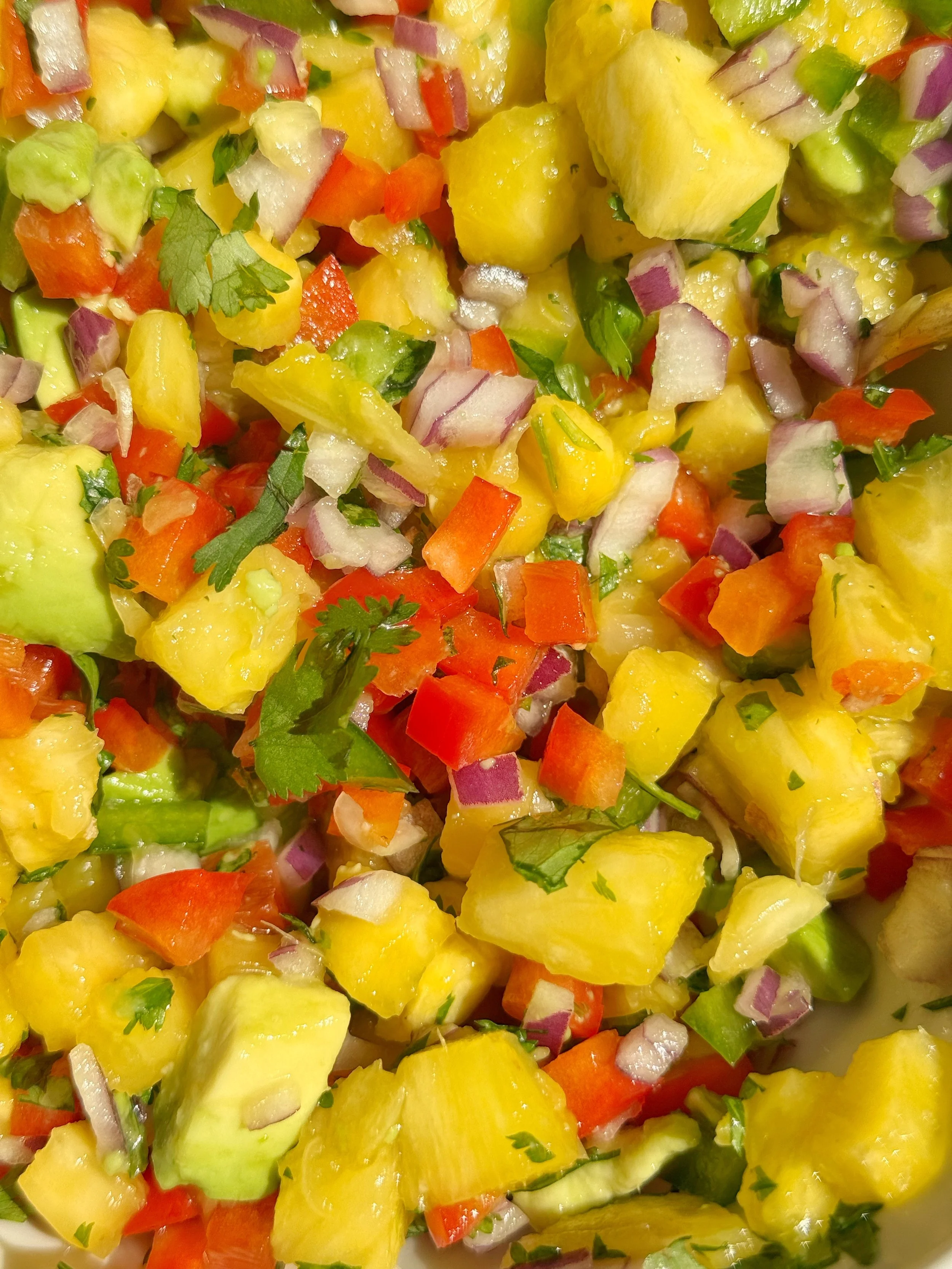 A close up shot of pineapple salsa with diced red onion, red pepper, jalapeños, avocado and fresh cilantro.