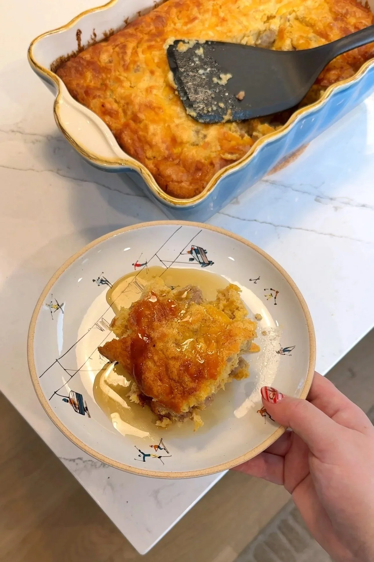 A baking dish with a breakfast casserole inside of it with a plate served with the same casserole topped with maple syrup and hot sauce. 