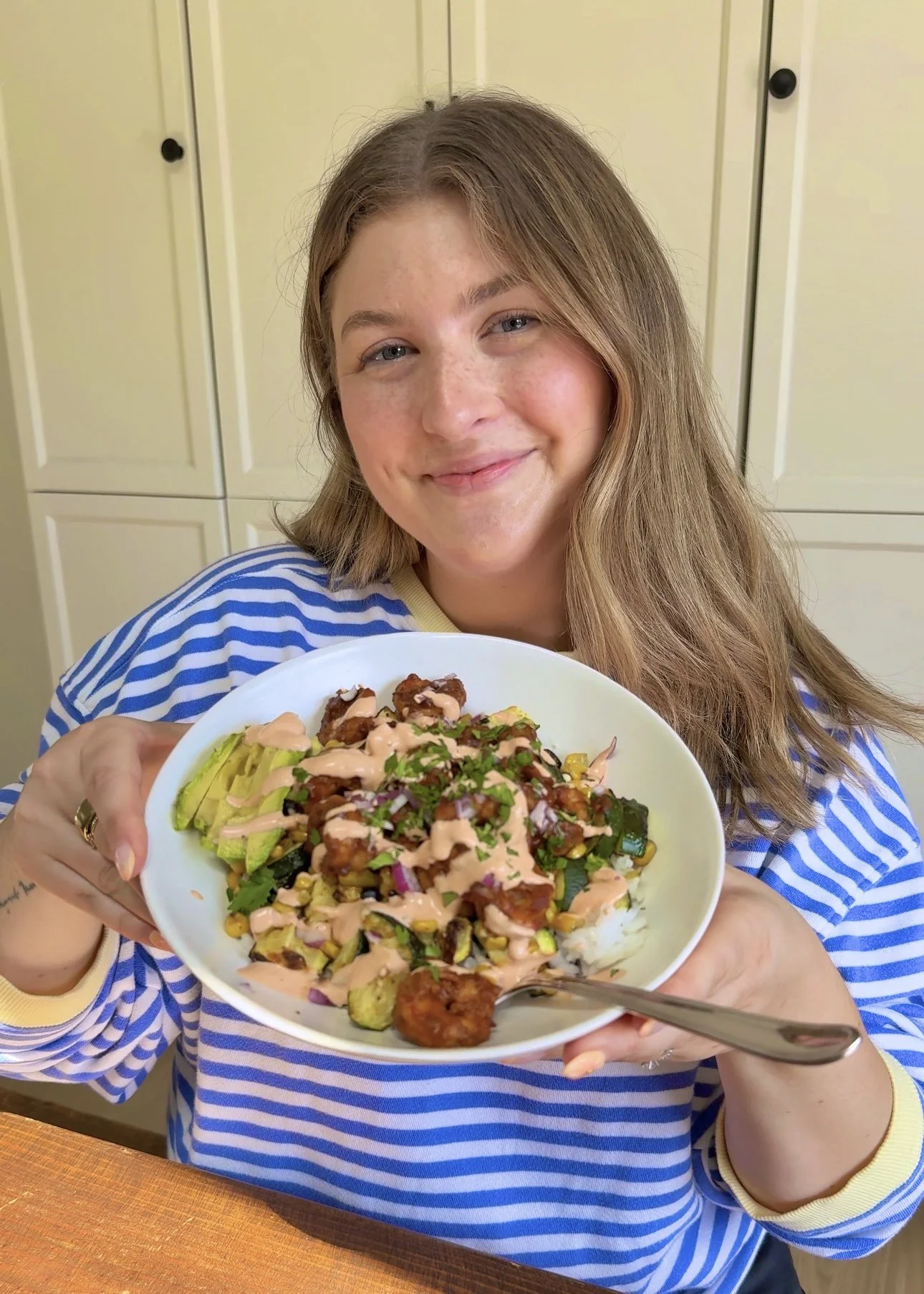 A bowl being held up that has shrimp, avocado, diced zucchini, corn, red onions with dressing and chopped cilantro on top.