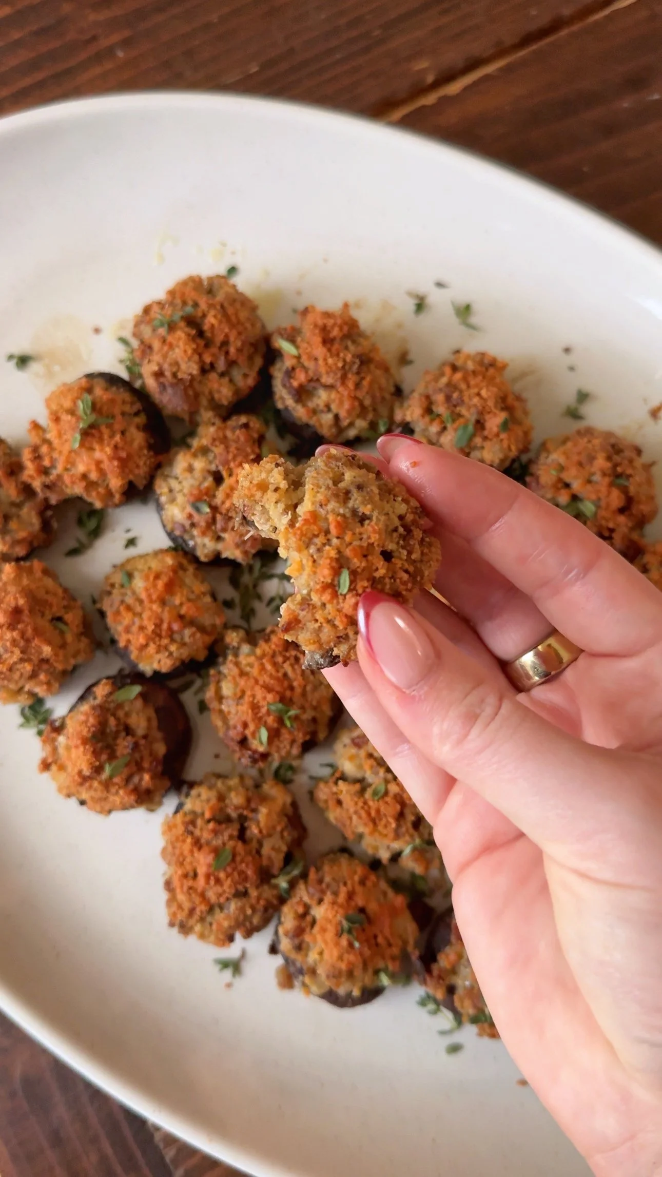 A platter of sausage & herb meatballs with a sprinkle of thyme on the top. One meatball is being held up in the air. 