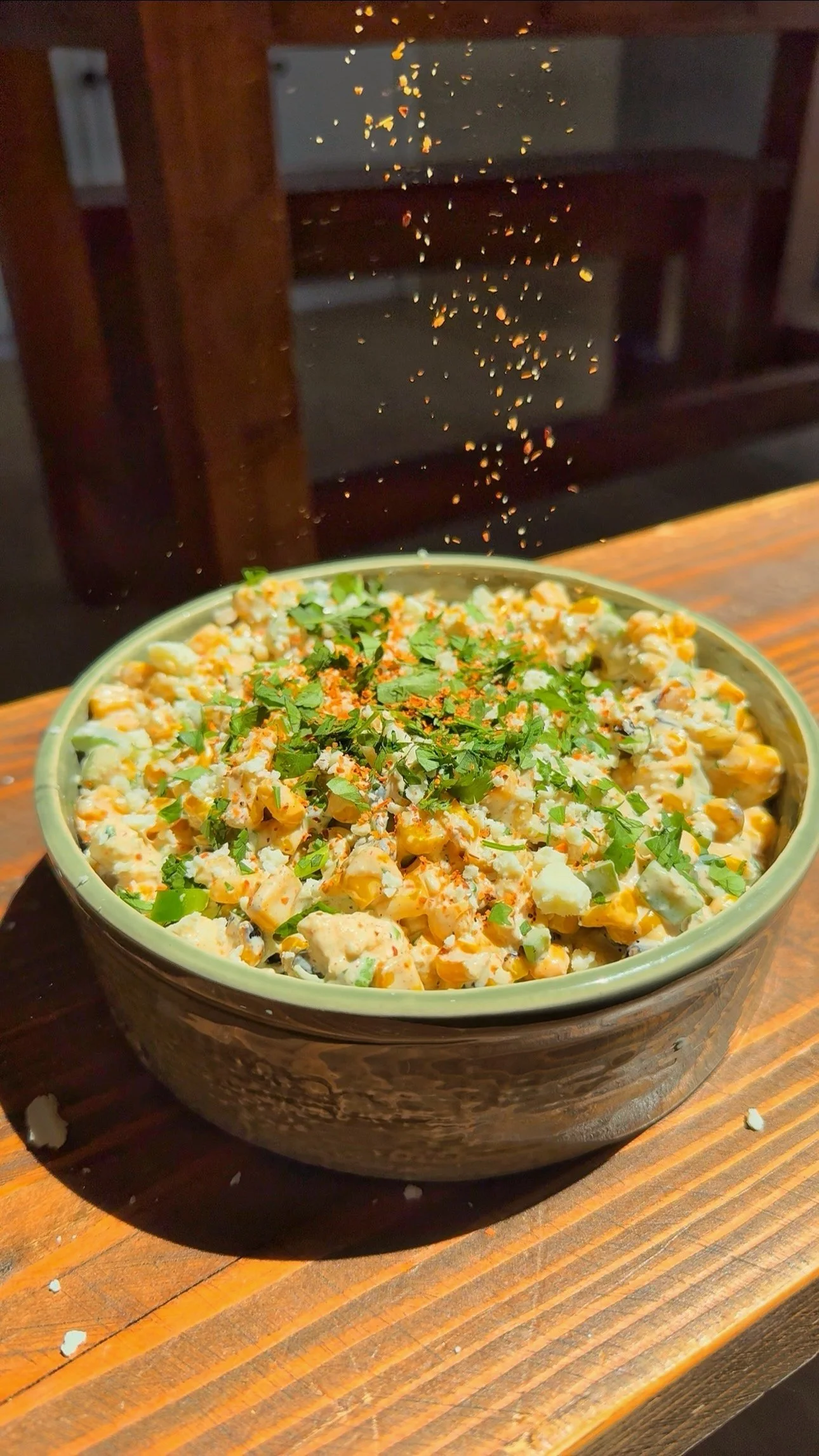 A bowl of corn dip with fresh chopped cilantro & Tajin on top.