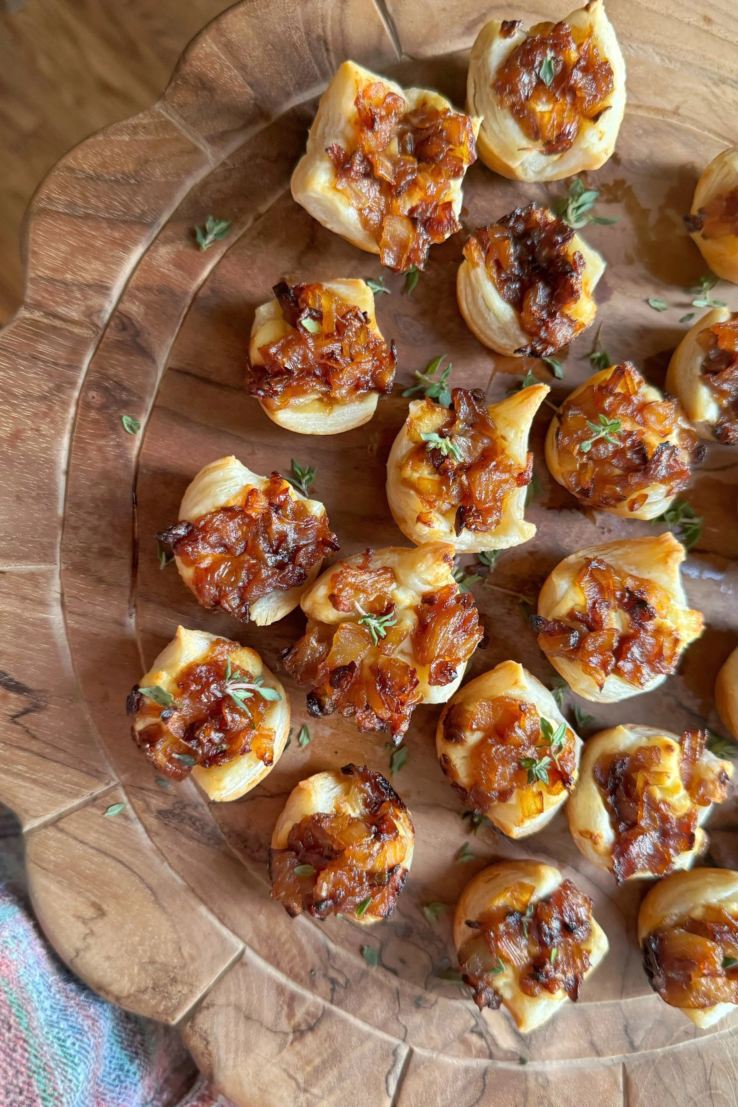 A cutting board with little pastry bites with caramelized onions and feta cheese. Topped with fresh thyme.