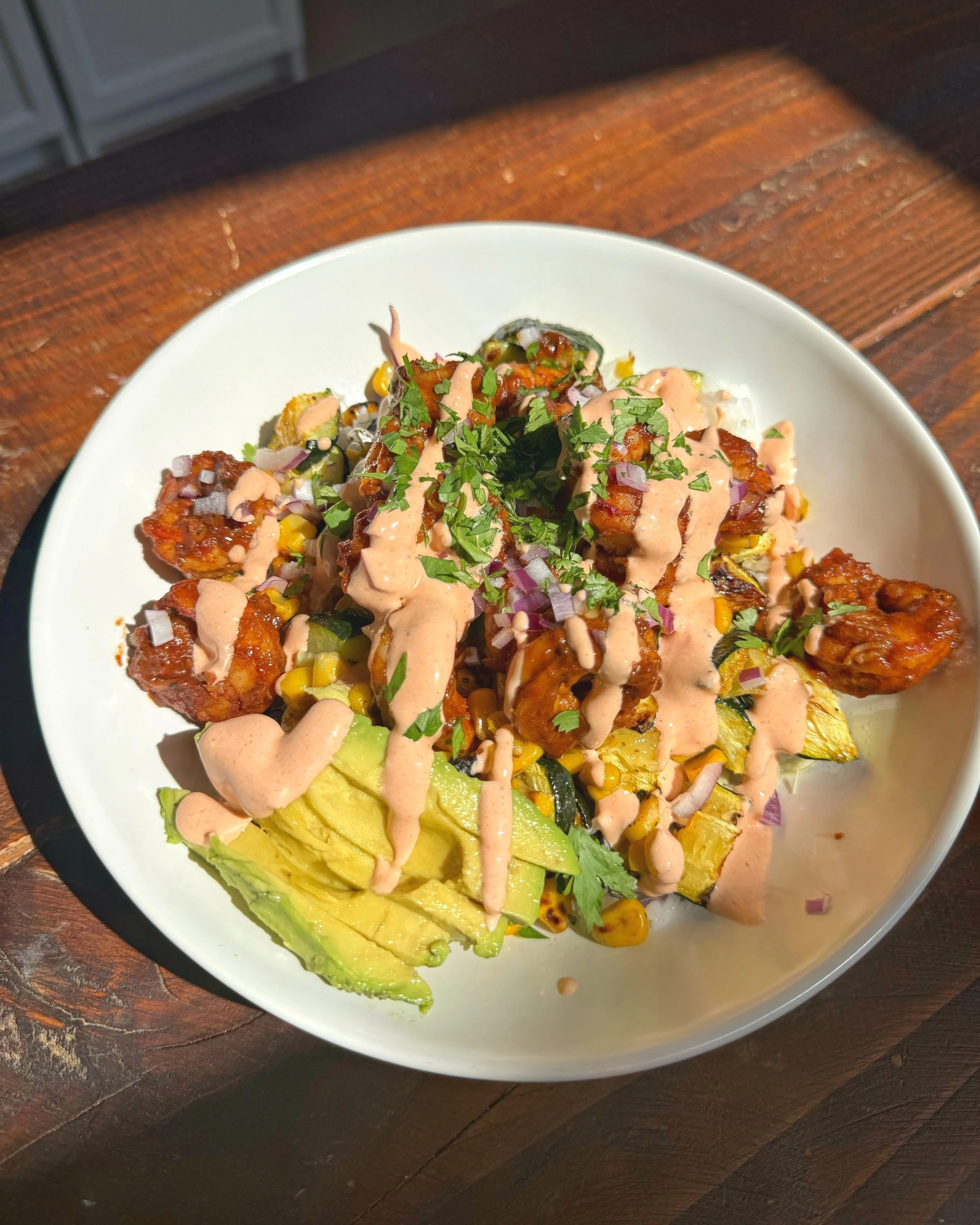 A bowl of shrimp, avocado, diced zucchini, corn, red onions with dressing and chopped cilantro on top.