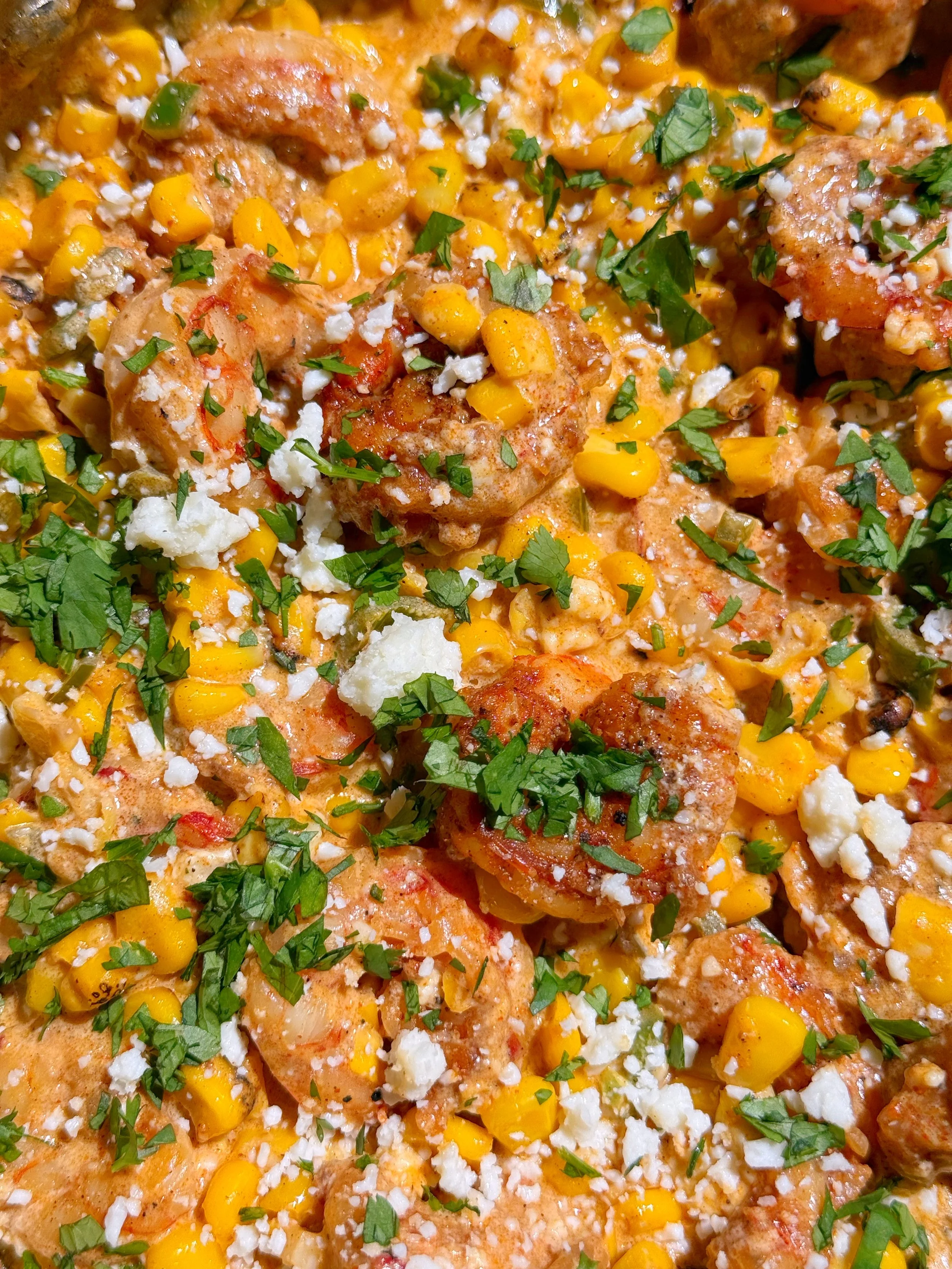 A close up shot of creamy corn & shrimp mixture with cotija cheese and fresh cilantro on top.