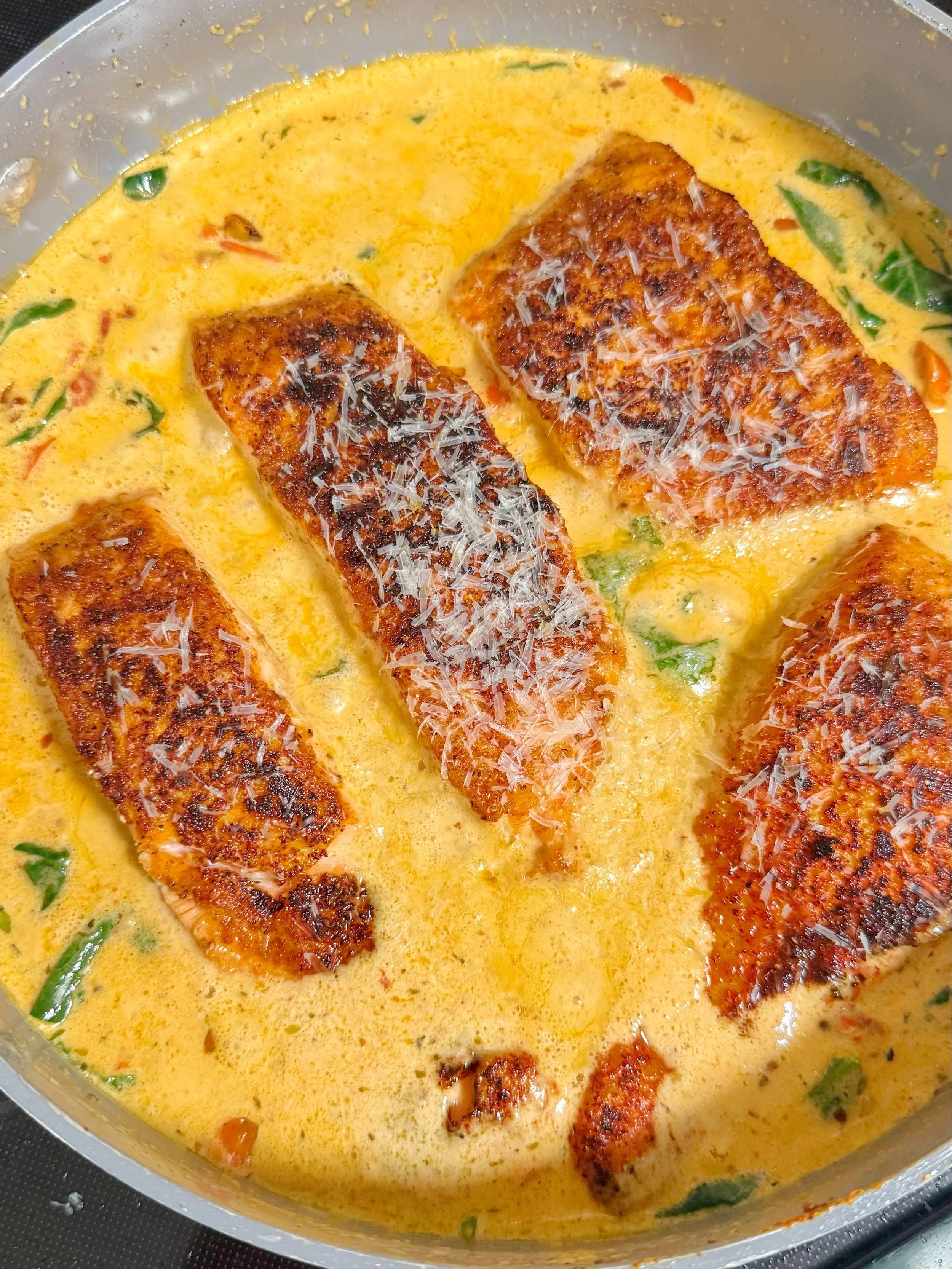 A pan with Tuscan salmon in a creamy sauce with grated cheese on top.