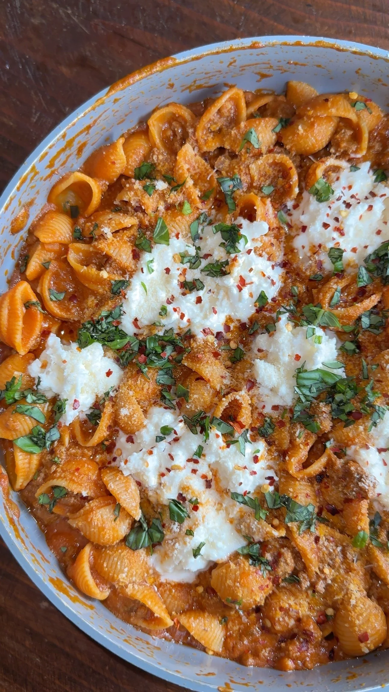 A pan of pasta shell noodles with burrata cheese & ground beef in a tomato base with fresh chopped basil and a sprinkle of red pepper flakes on top.