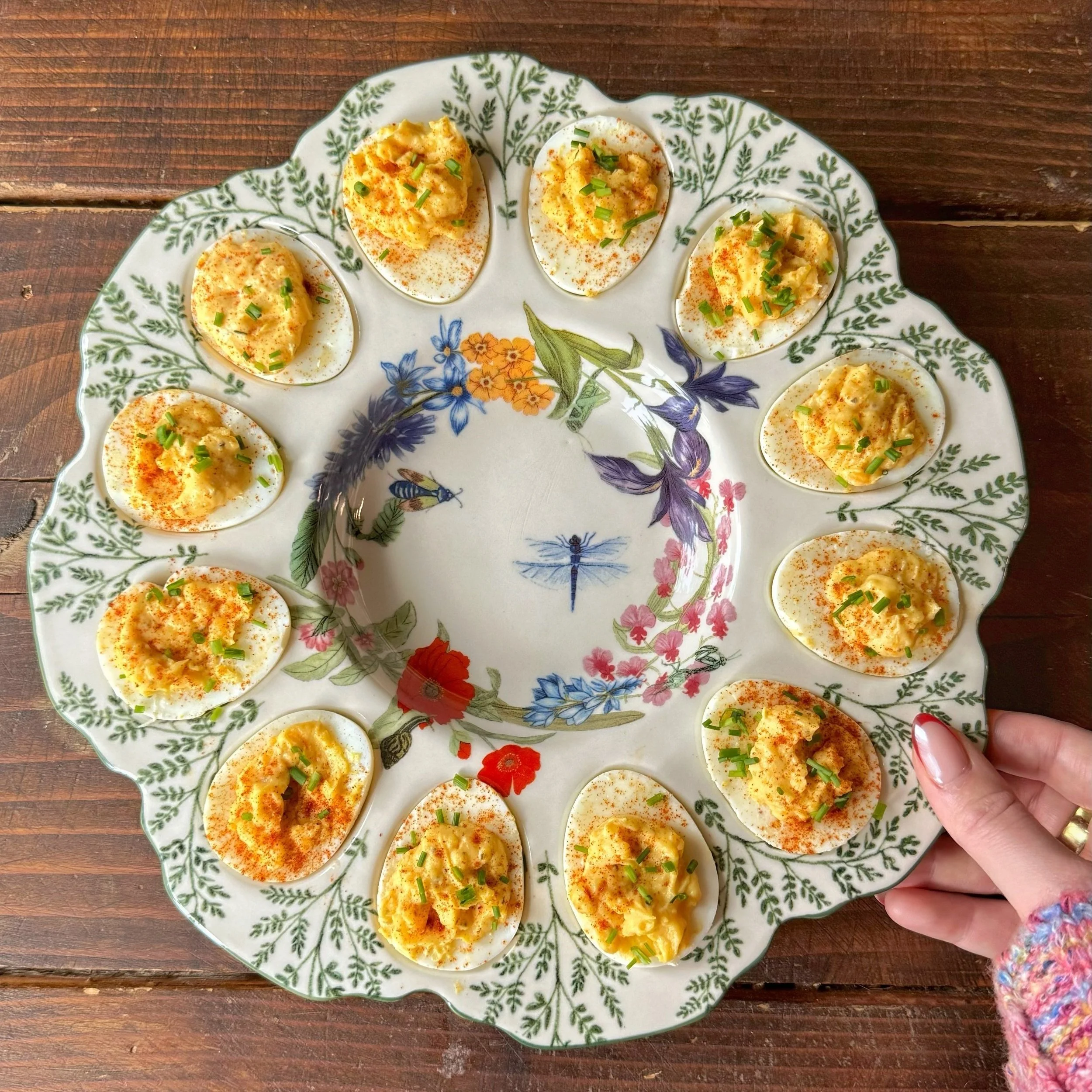 A beautiful plated on a wood table filled with deviled eggs with sprinkled paprika and chopped chives.
