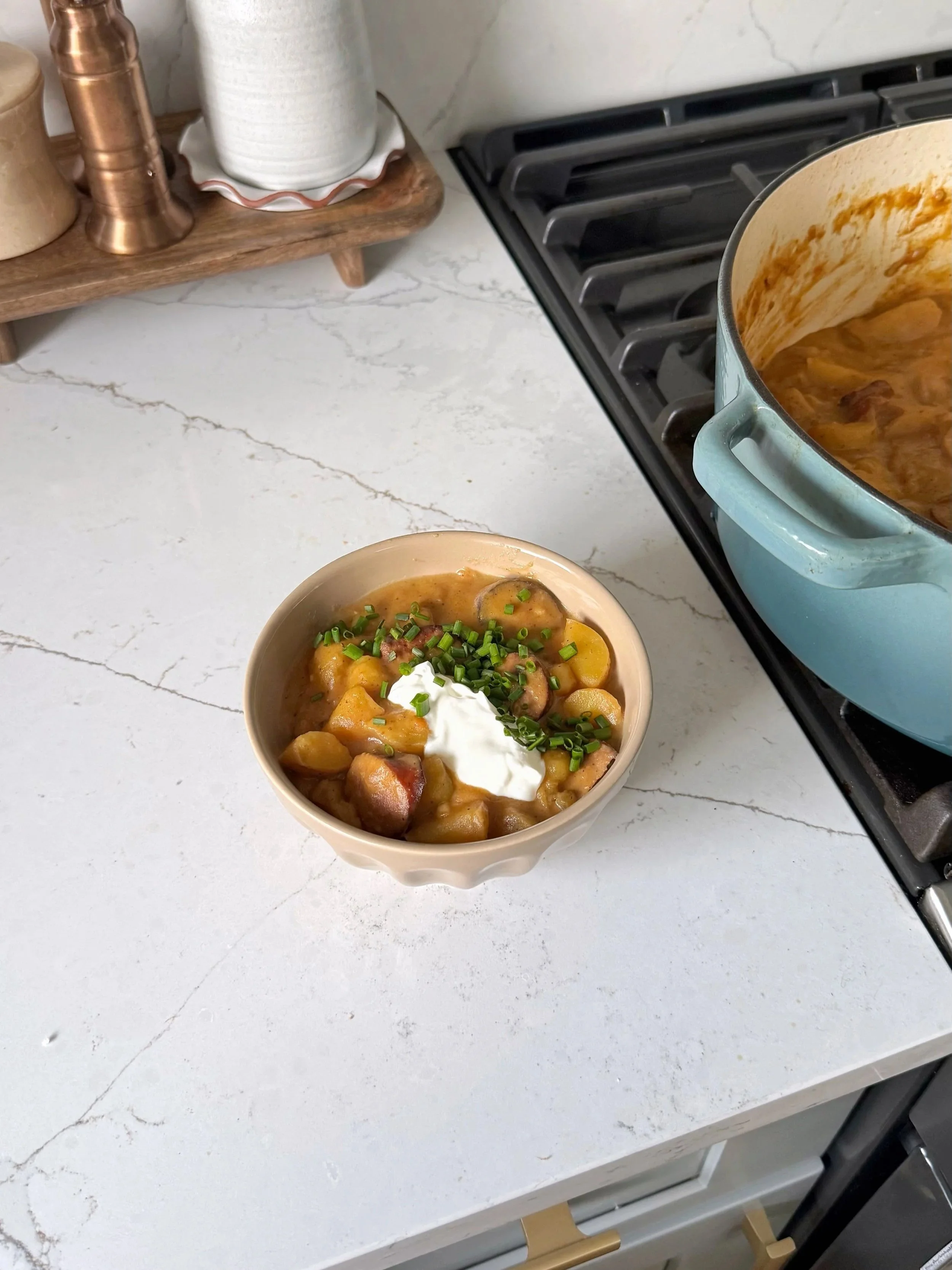  A bowl of potatoes & Kielbasa sausage in a creamy sauce topped with sour cream and chopped green onions.
