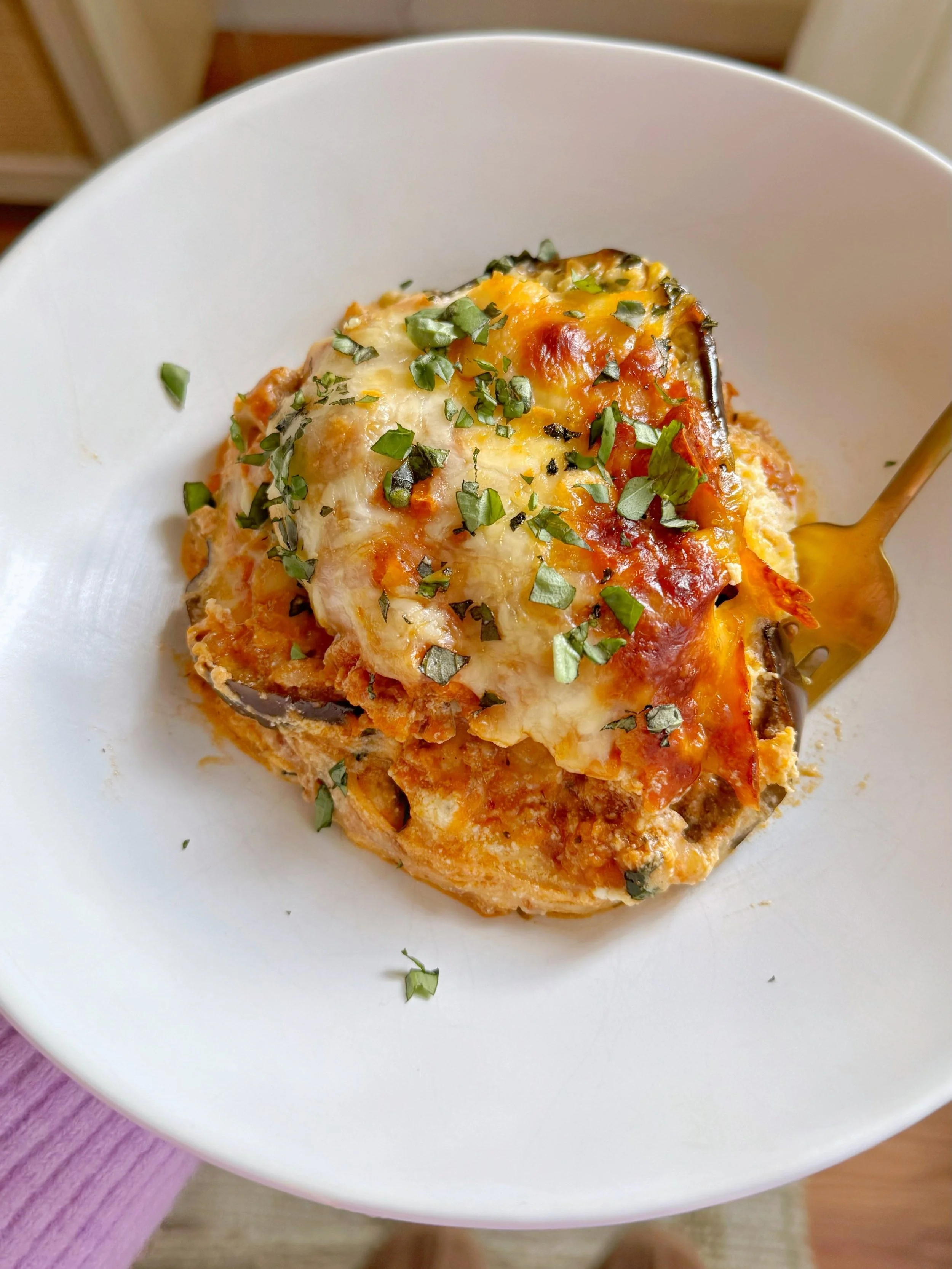 A bowl of eggplant lasagna topped with fresh shredded cheese and chopped basil.