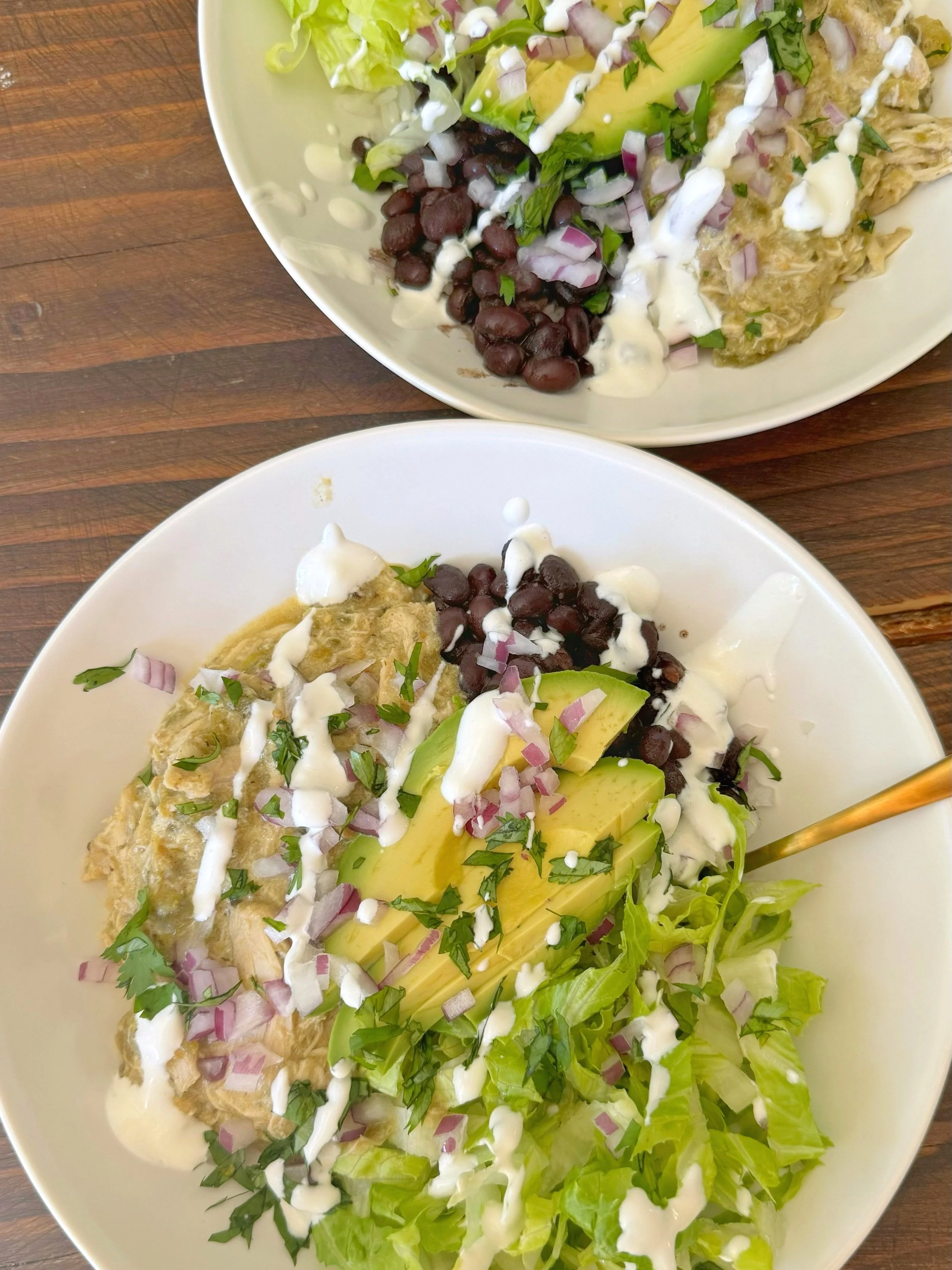 Two bowls of chicken, lettuce, black beans, avocado, chopped red onion and cilantro with sour cream drizzled on top. 