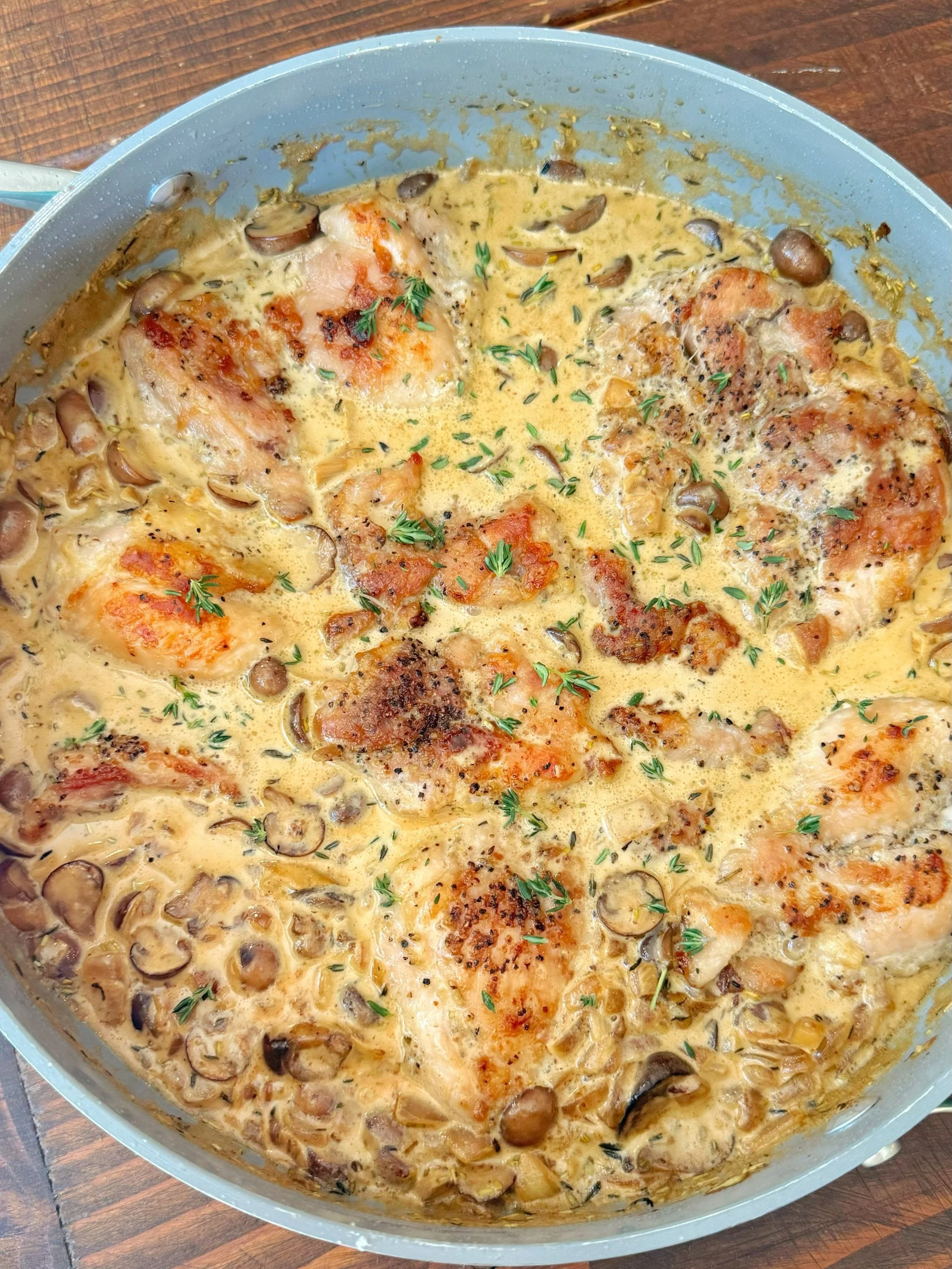 A pan of creamy chicken with mushrooms over a bed of rice topped with fresh thyme. 