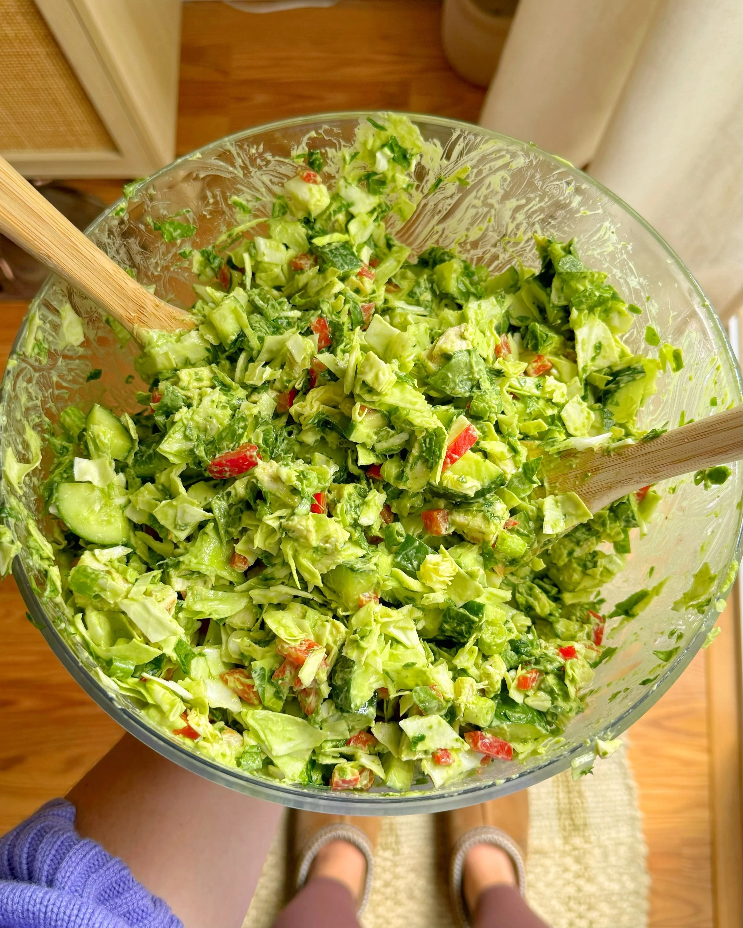A big serving bowl of a salad that has green cabbage, cucumbers, green onions, spinach and bell peppers with a green dressing mixed into it.