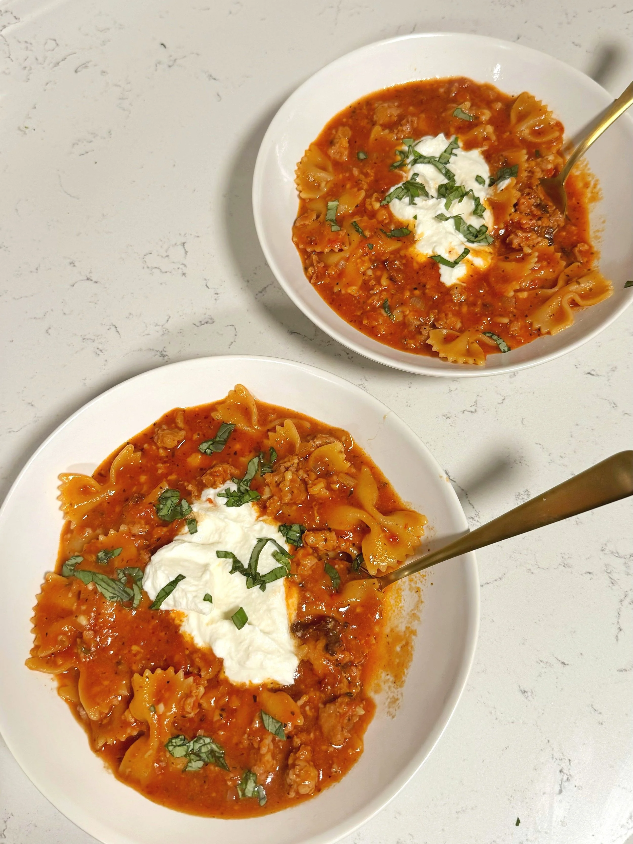 Two bowls of lasagna soup with a scoop of ricotta cheese and fresh basil on top.