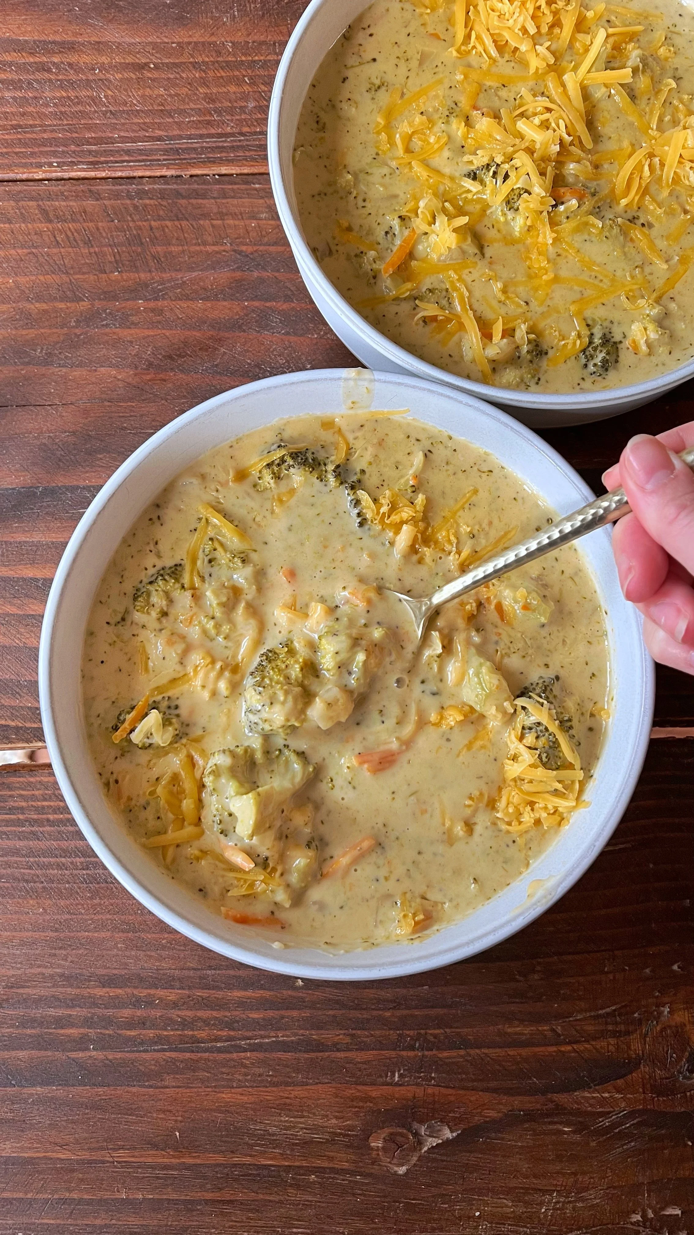 Two bowls of broccoli cheddar soup with grated cheese on top.