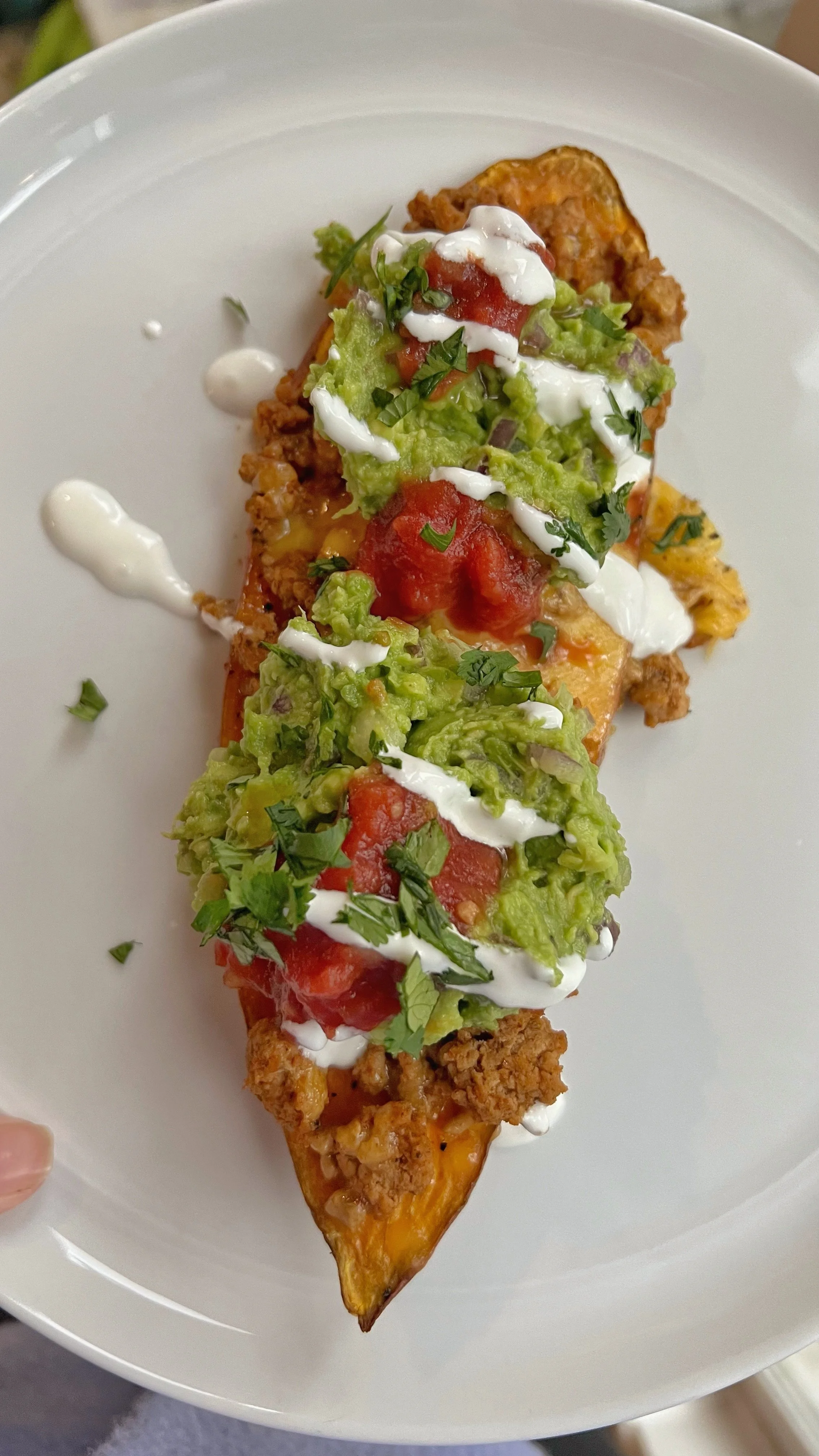 A plate with an open face sweet potato with ground turkey, melted cheese, guacamole, salsa, sour cream and fresh cilantro. 