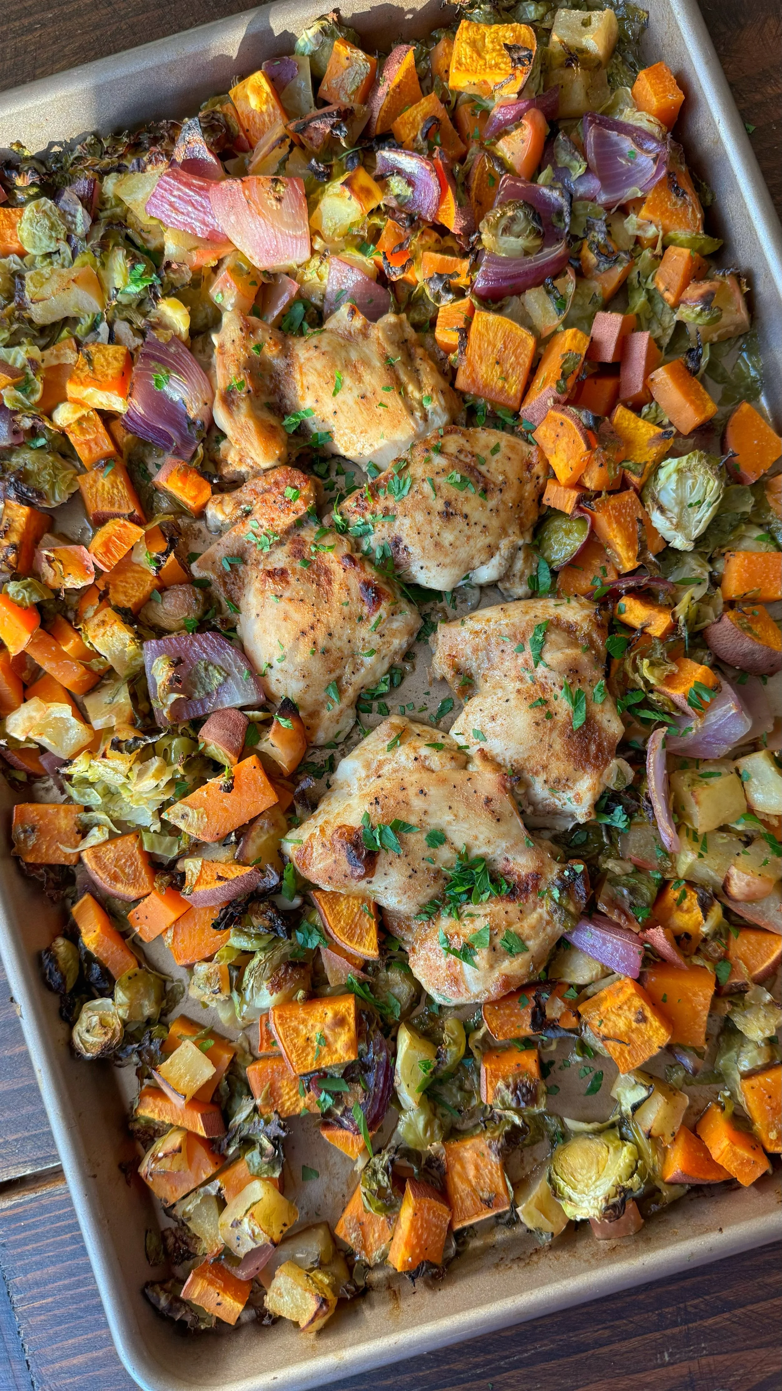 A baking sheet of glazed chicken with roasted carrots, onion and Brussels sprouts.