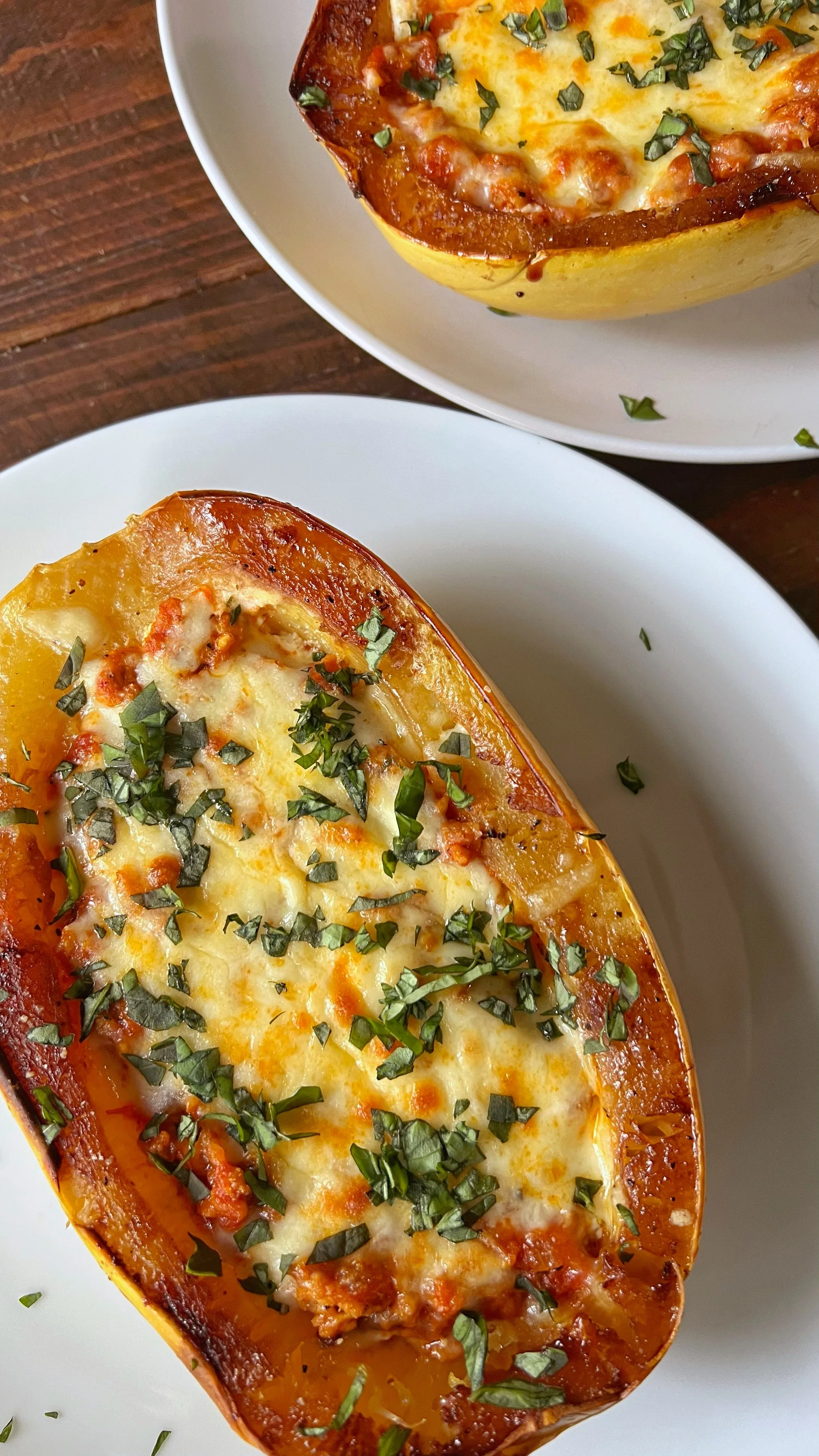 A plate with open faced squash filled with ground chicken sausage, melted cheese and fresh chopped basil.
