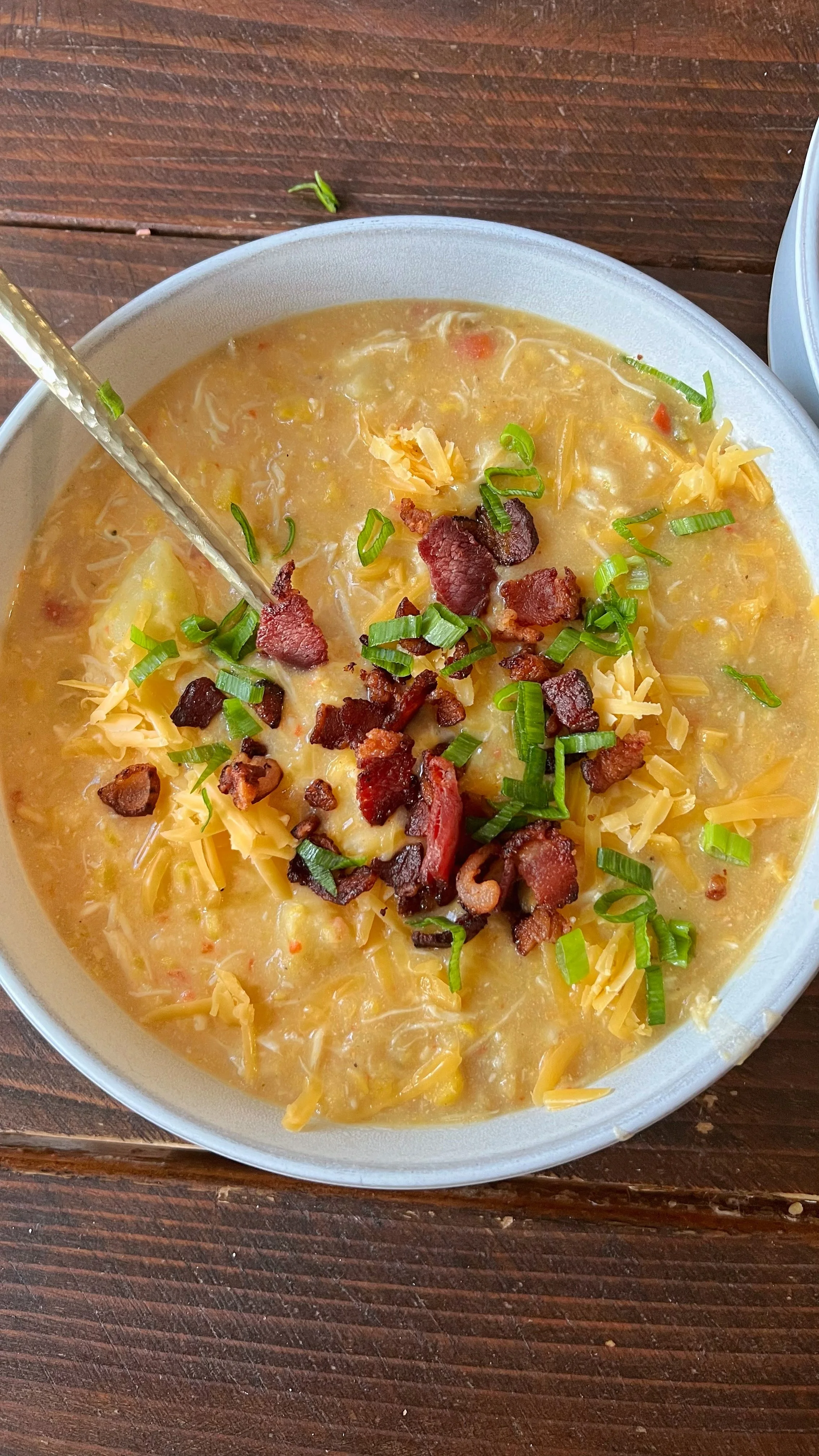 A bowl of corn chowder with chicken, cheese topped with bacon & green onions.