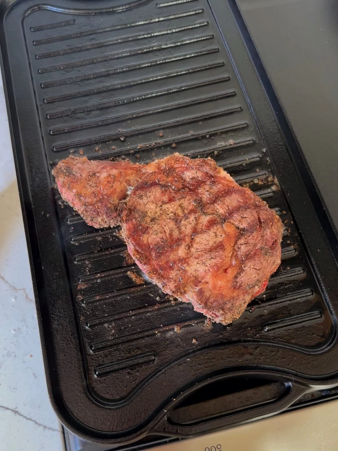 A large steak cooking on a grill pan.