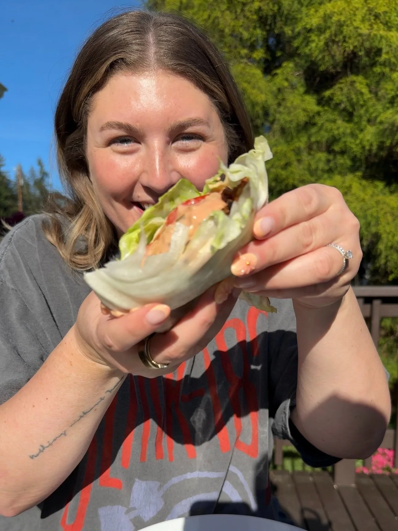 A burger with tomato and dressing wrapped in lettuce that is hand held.