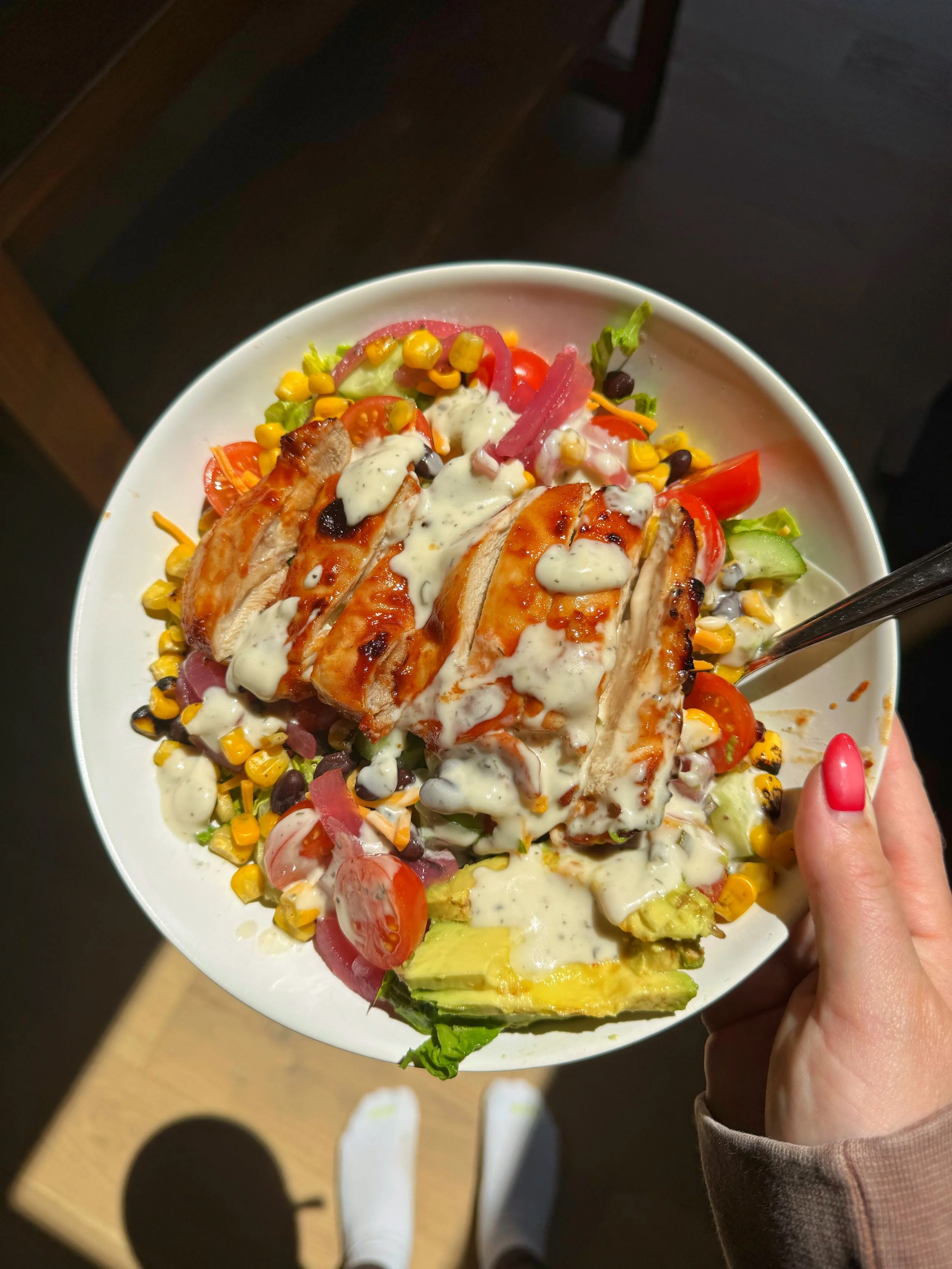 A bowl of air fried BBQ chicken salad with corn, avocado, black beans & tomatoes