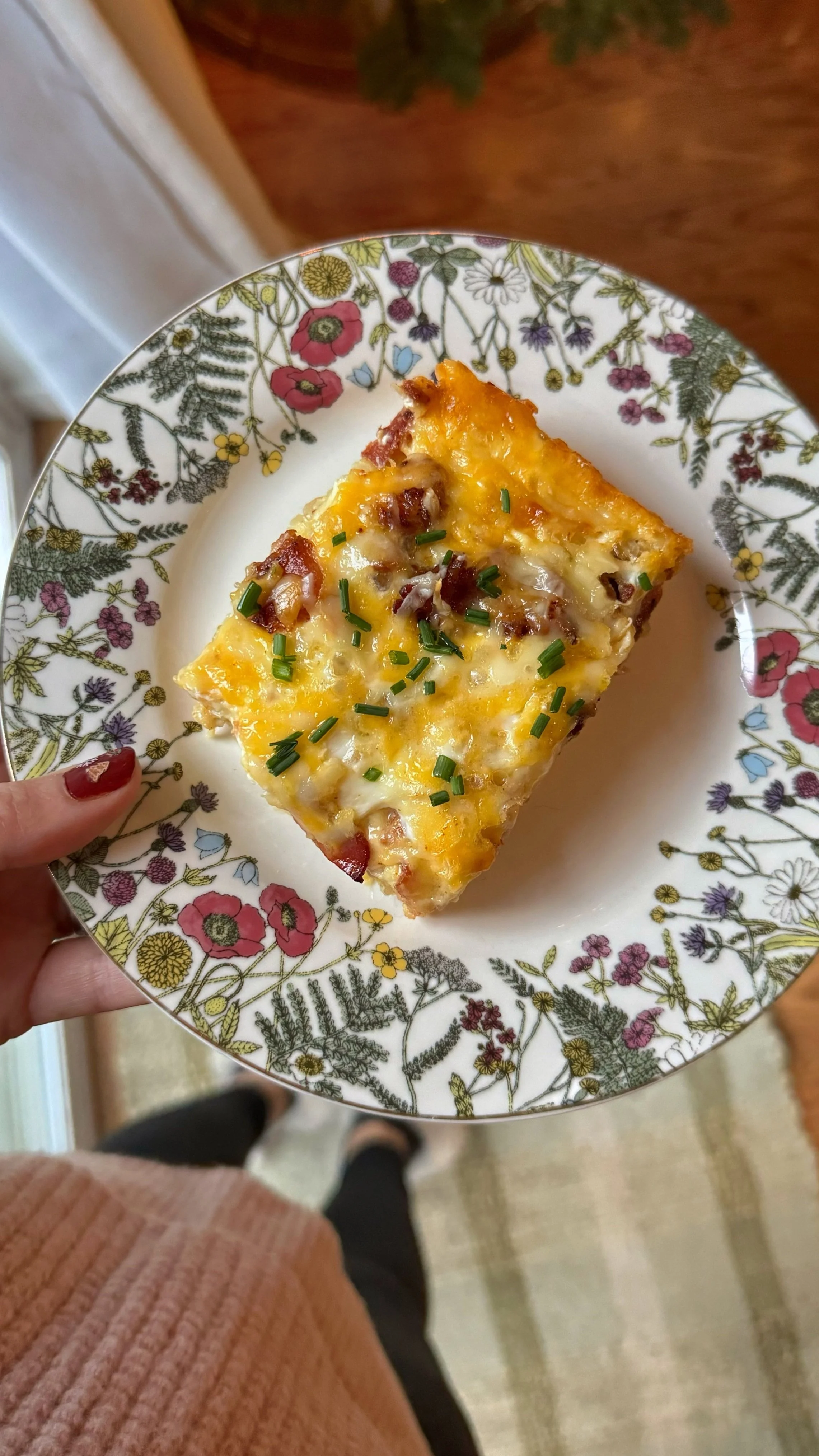 A breakfast casserole with egg, bacon and cheese topped with chopped chives served on a plate.
