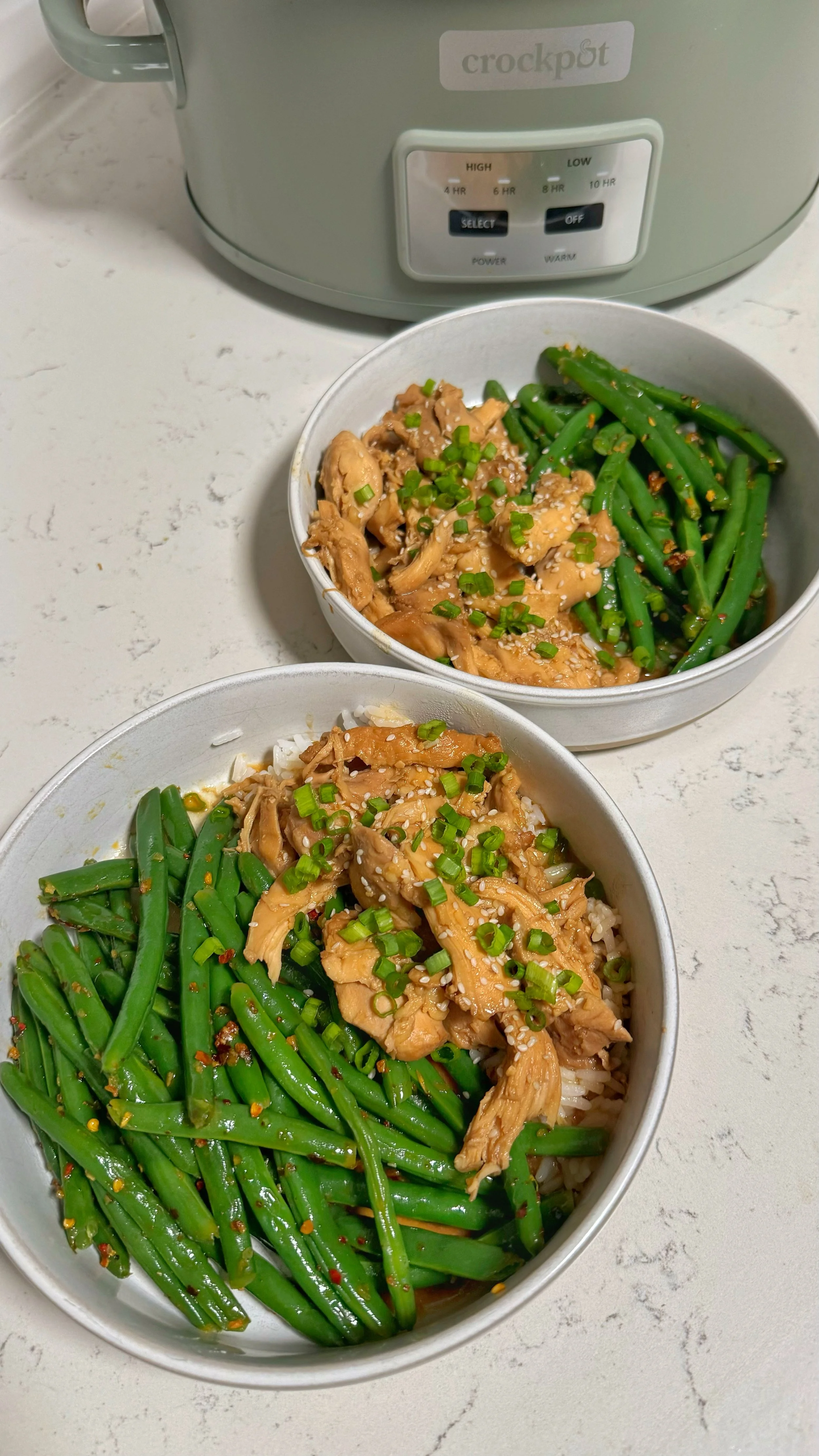 Two bowls of teriyaki chicken and a side of green beans on a bed of rice with chopped green onions & sesame seeds on top. 