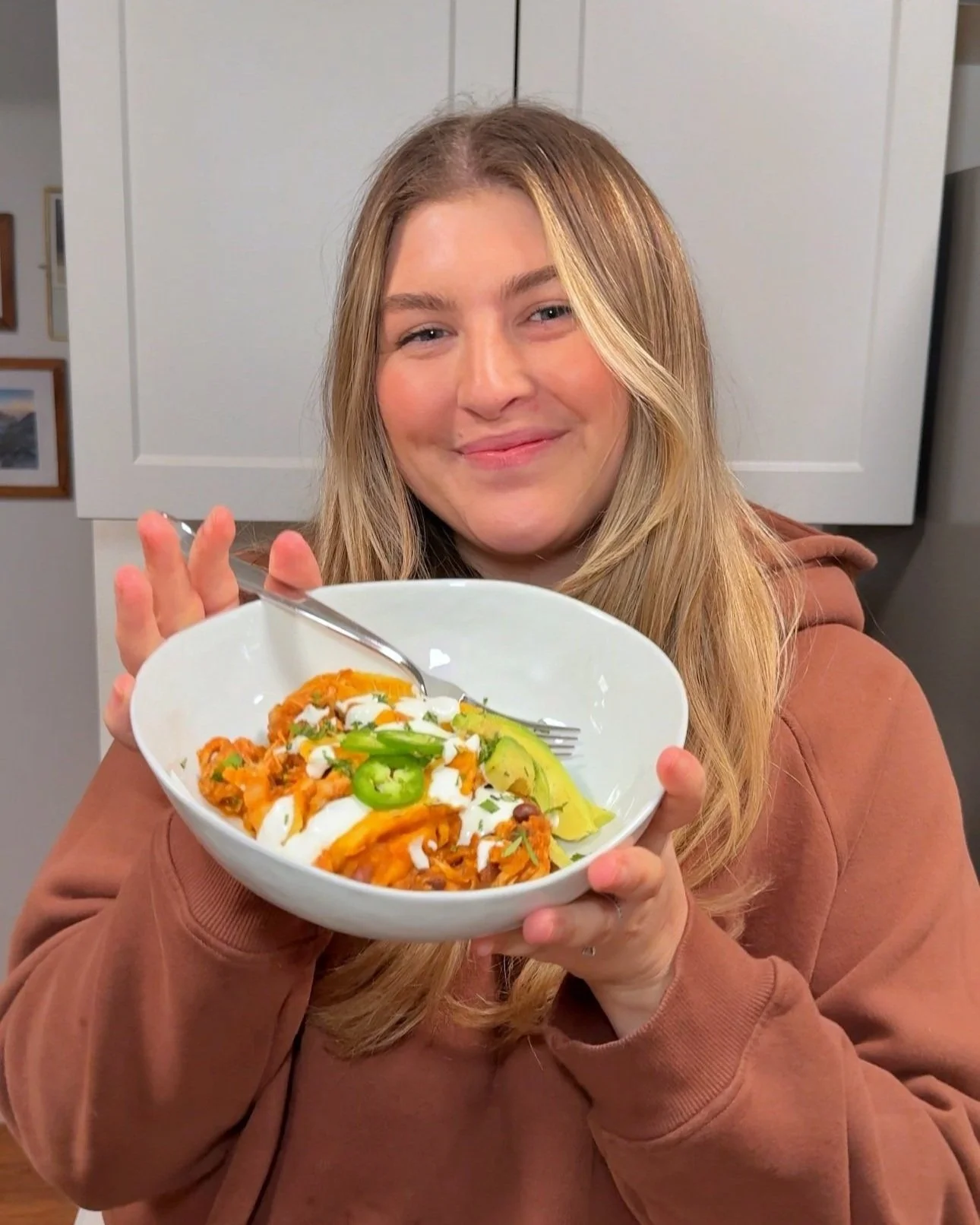 A bowl being held with chicken enchiladas with sliced avocados, sour cream, Jalapeños & cilantro on top. 