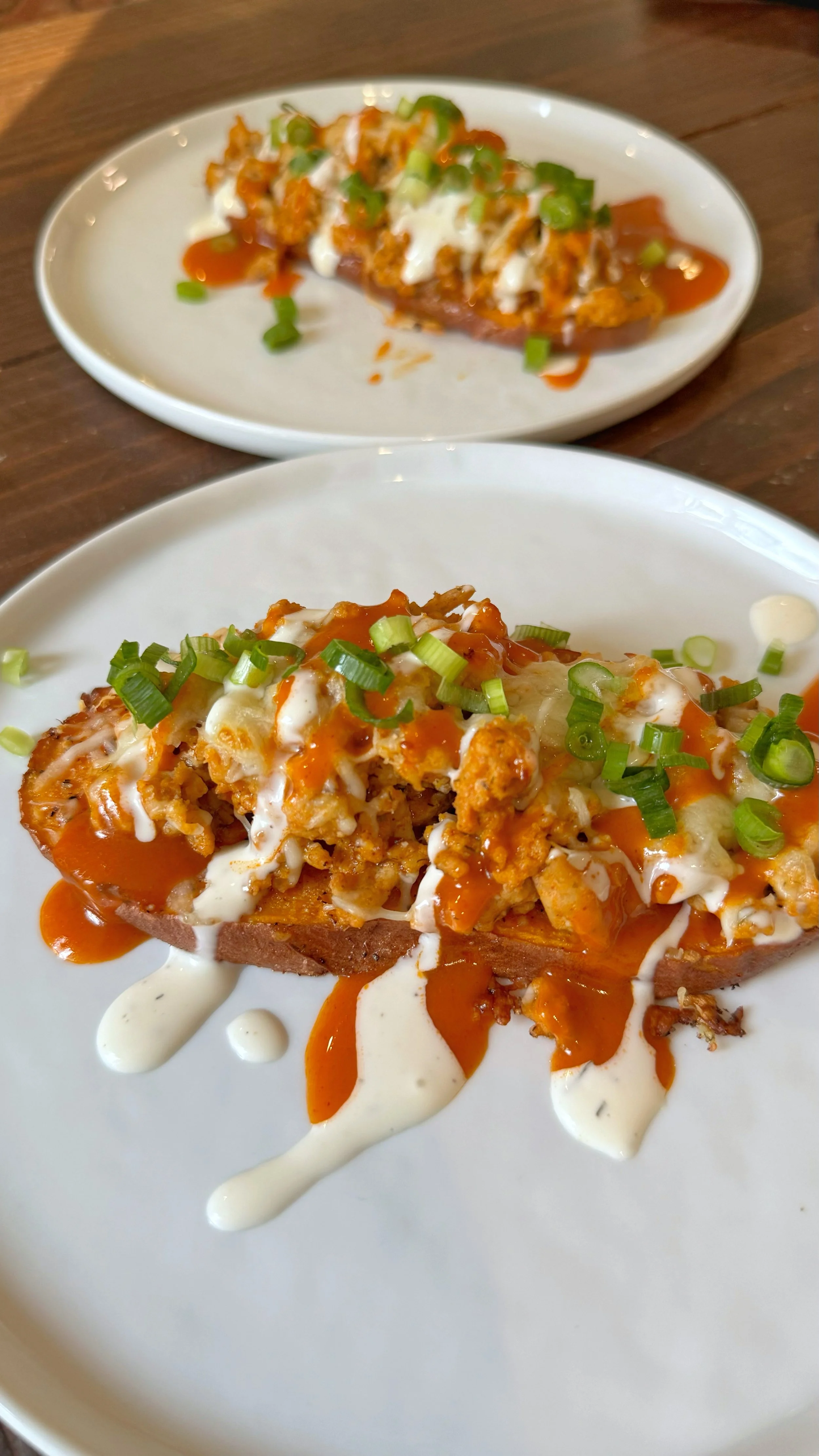 Two plates of sweet potato with ground chicken & buffalo sauce topped with chopped green onions and a drizzle of dressing.