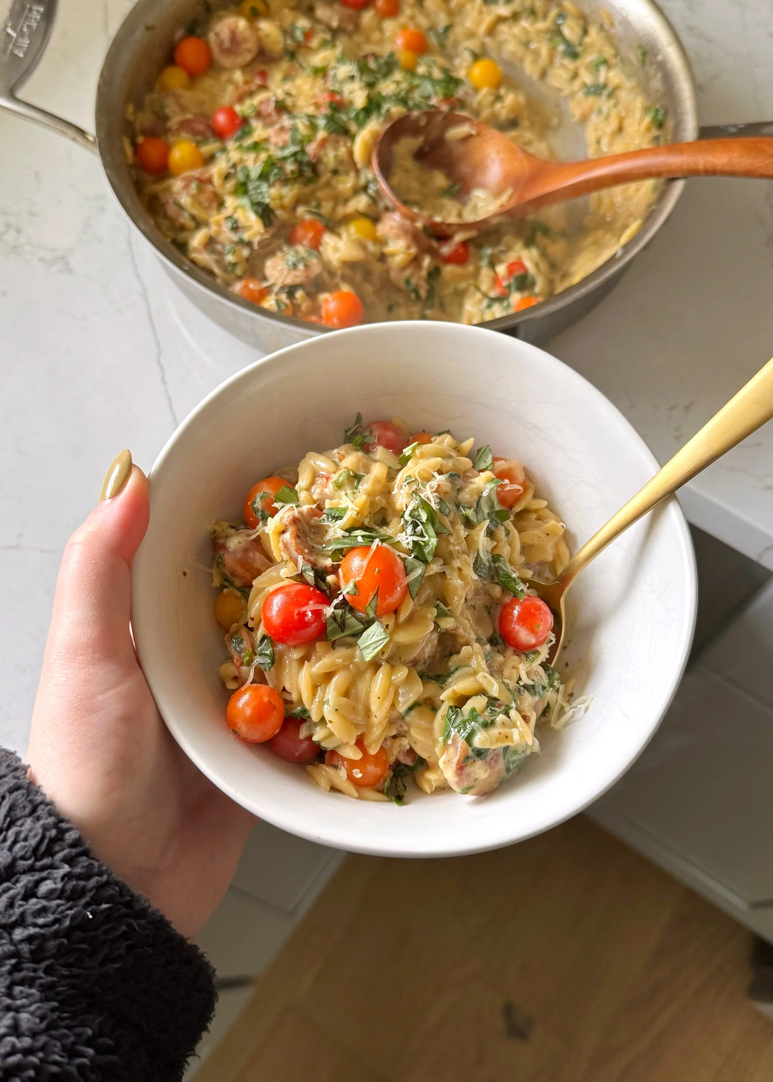 A bowl of orzo with sausage, mini tomatoes, and baby spinach in a creamy sauce topped with fresh basil and grated cheese.