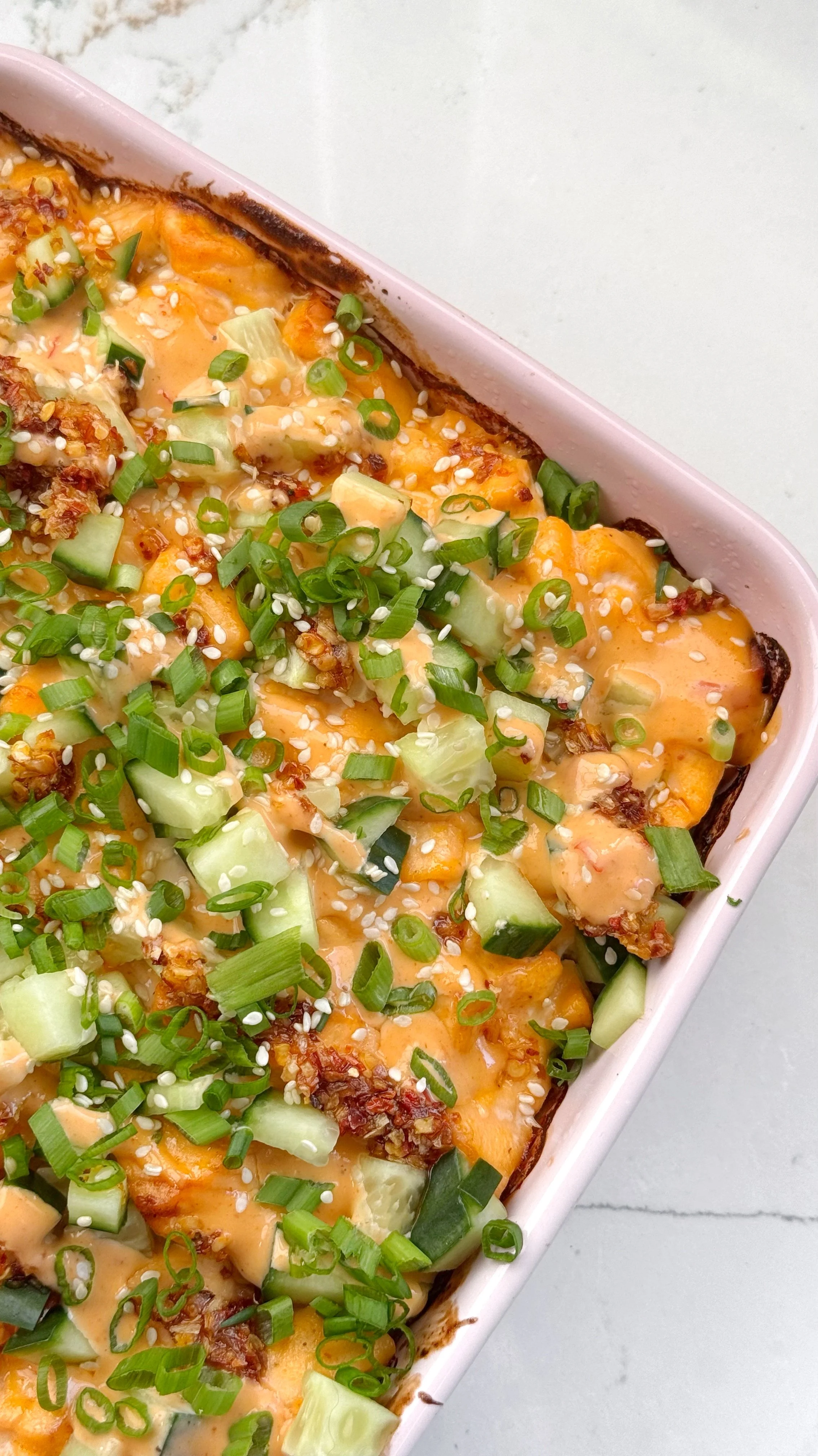 A close up shot of a casserole dish with salmon bake topped with fresh diced cucumbers, chopped onions, and sesame seeds.