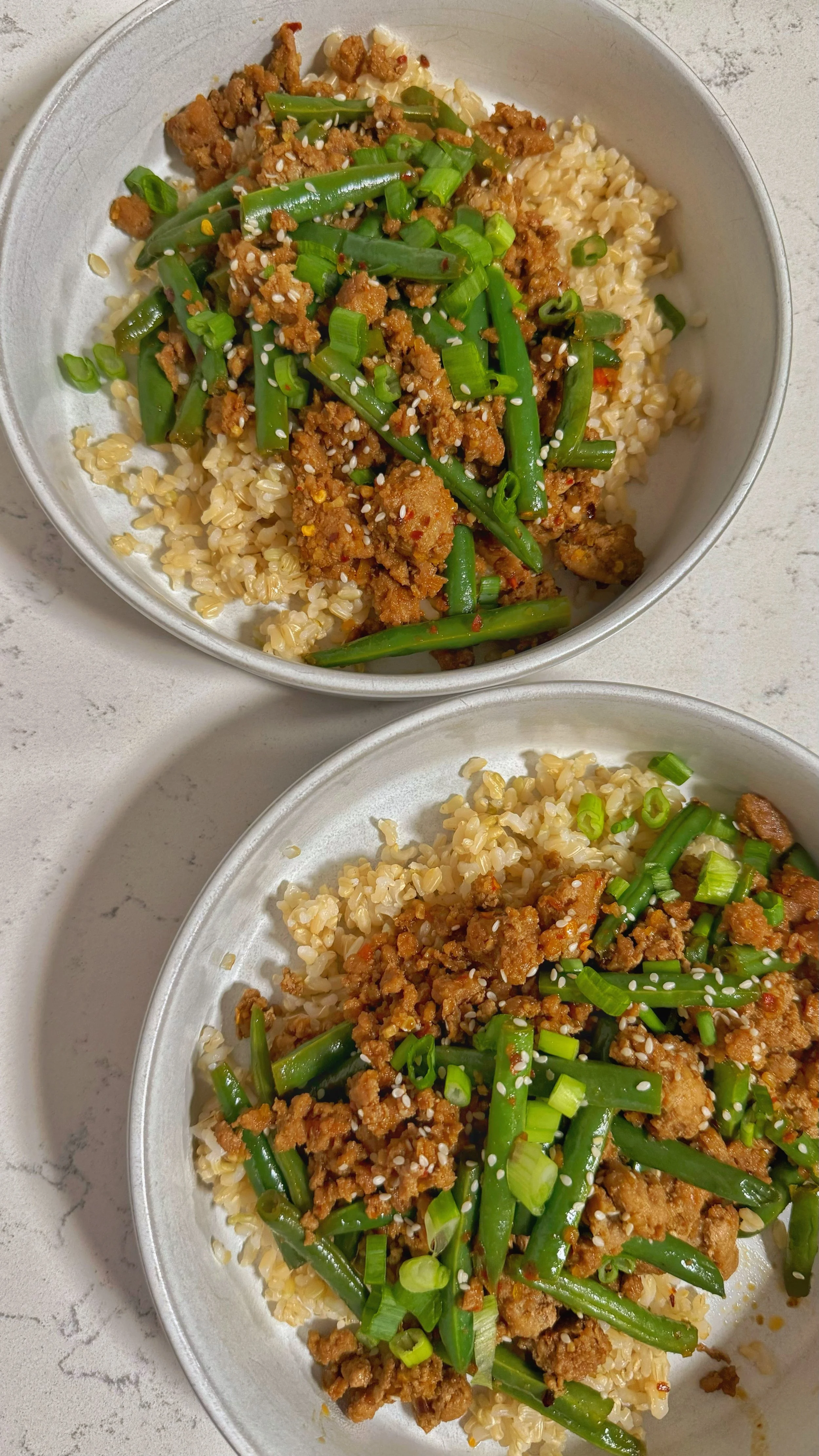 Two bowls of ground turkey and green beans over rice with chopped green onions and sesame seeds on top.