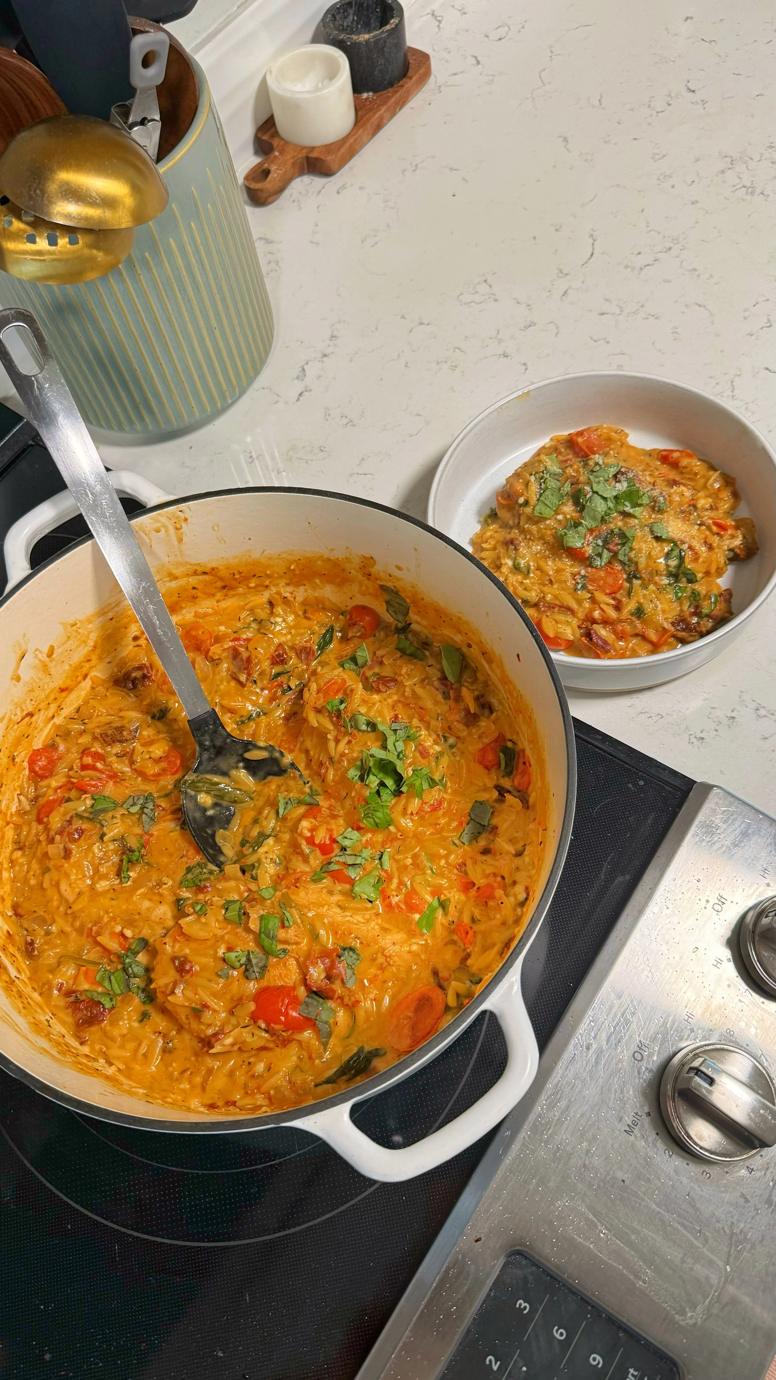 A pot and a bowl of creamy orzo with chicken and tomato, topped with fresh basil. 