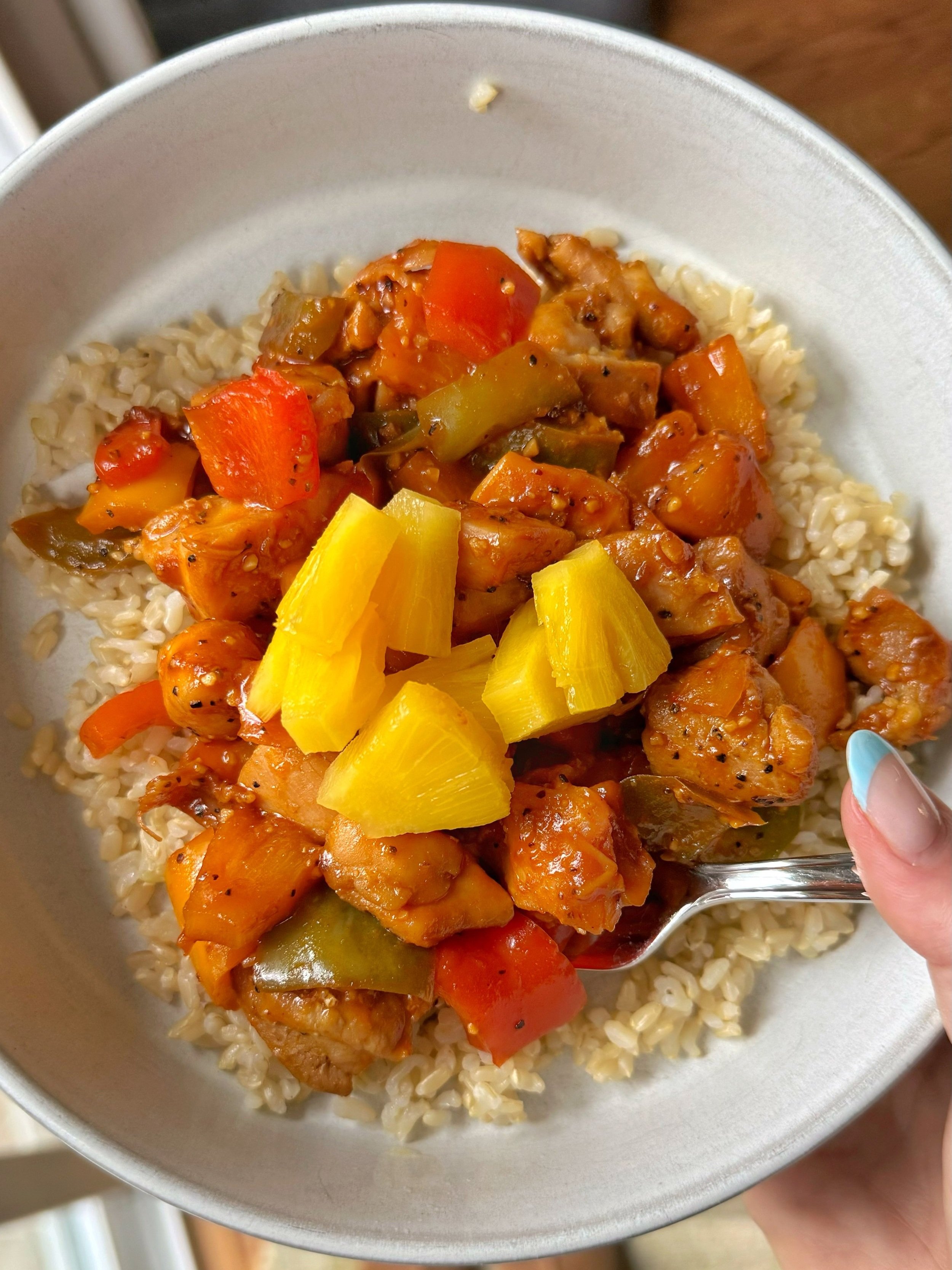 A bowl of pineapple chicken and peppers over rice.