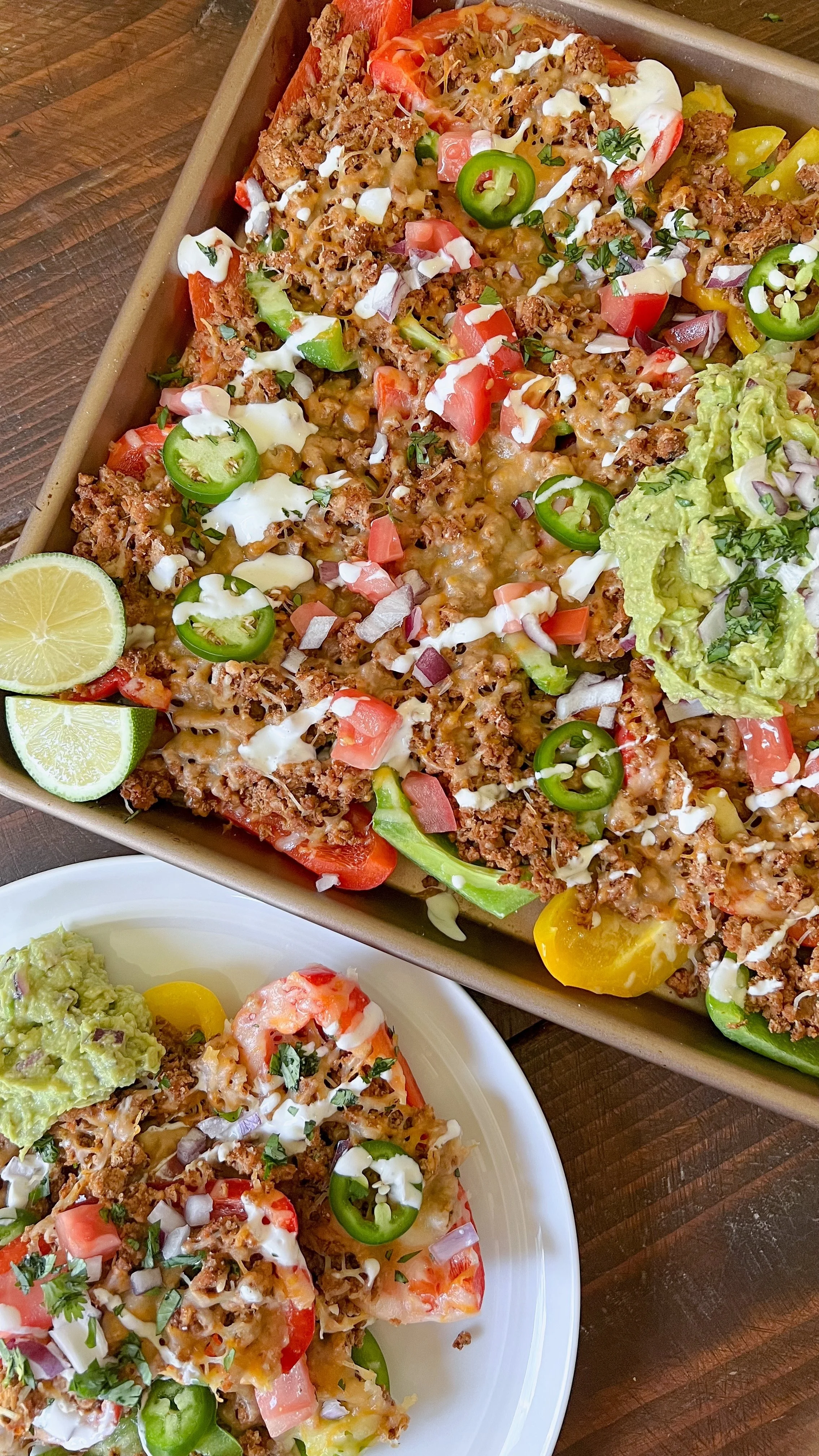 A plate of bell pepper nachos with guacamole, red onions, jalapeños, cilantro and sour cream on top. Fresh slices of lime on the side. 