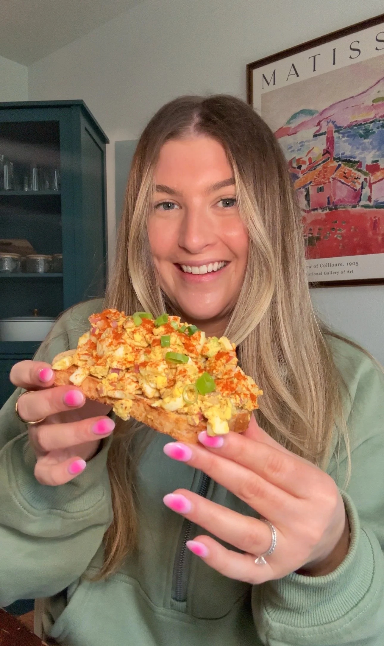 Cailee holding up an egg salad on a piece of bread topped with paprika and chopped green onions.
